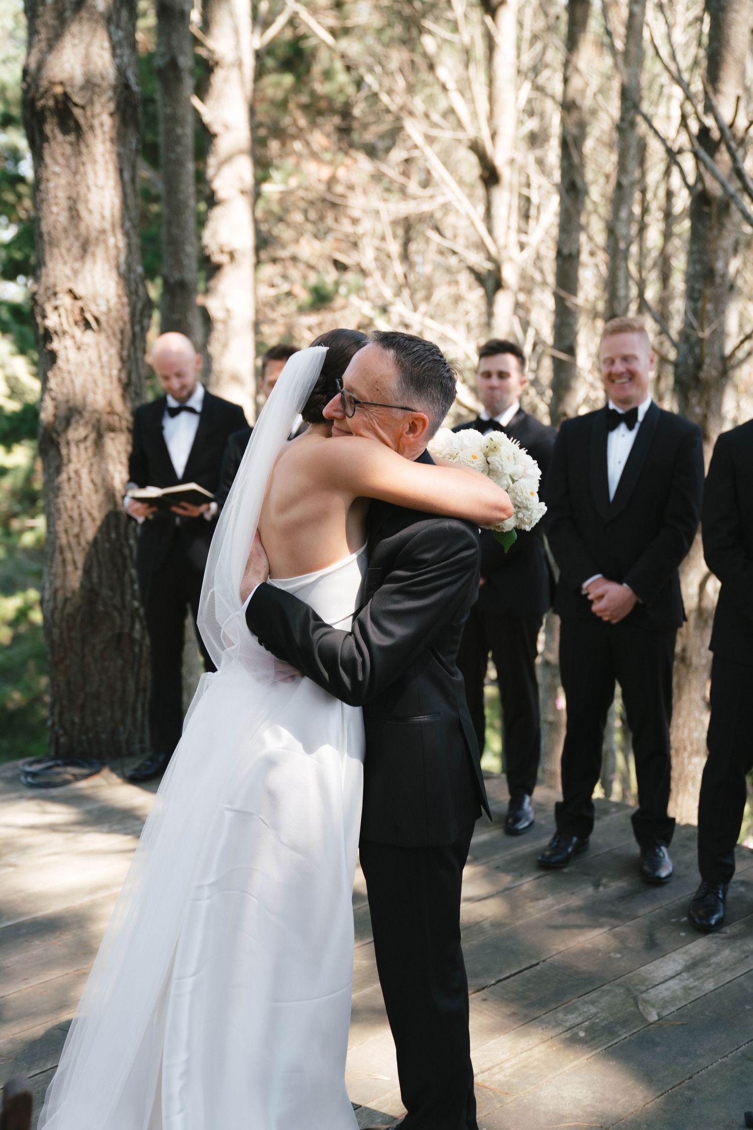 A tender embrace between newlyweds during their forest wedding ceremony as guests look on.