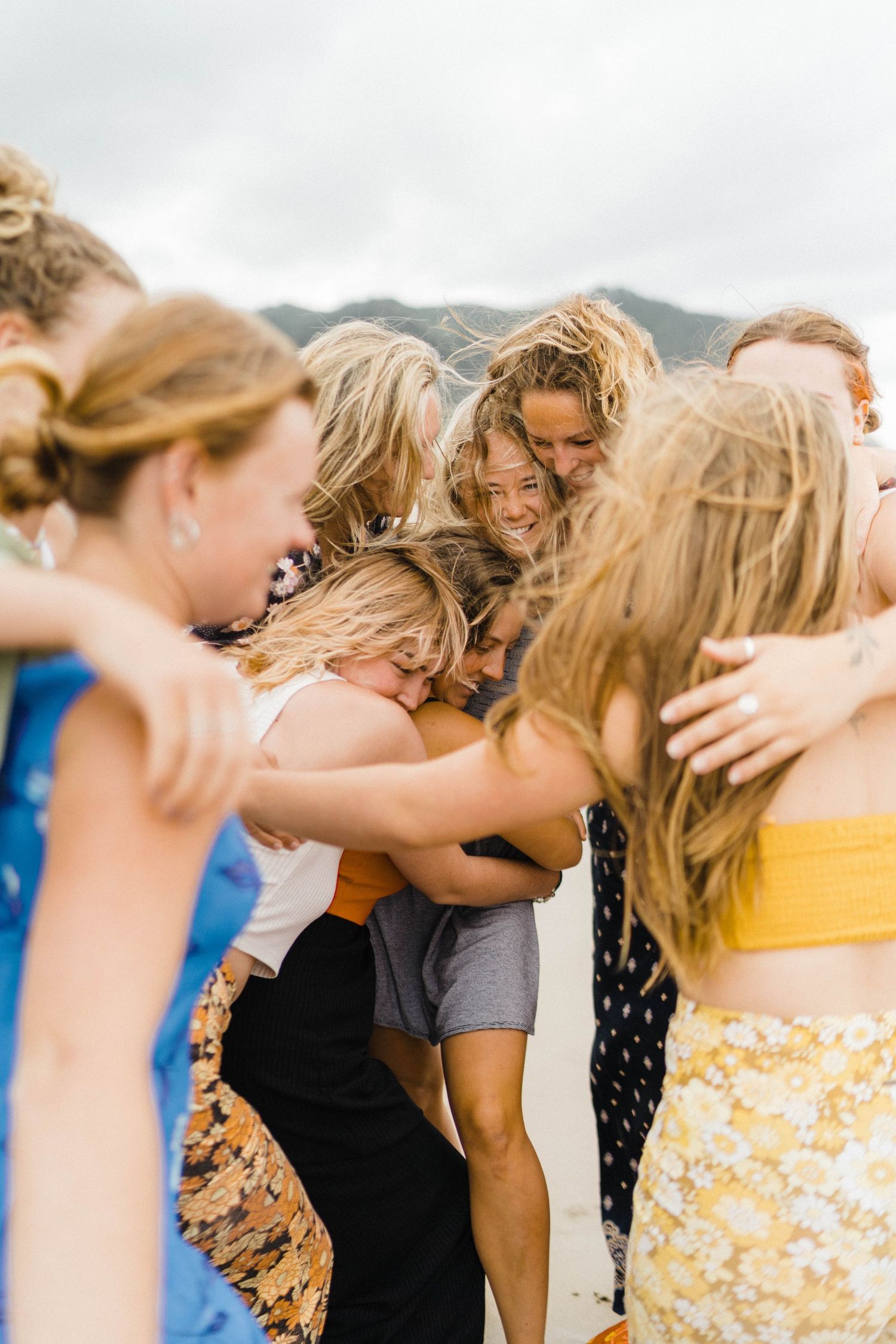 Group embracing in a close huddle outdoors with mountains in background.
