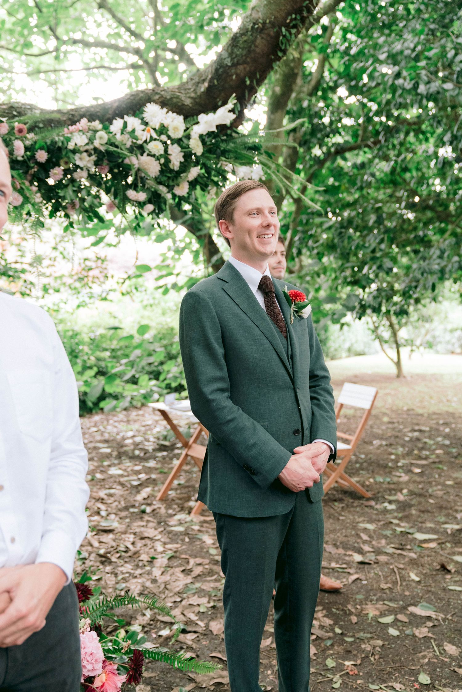 First look wedding photos in green garden setting with groom in dark suit reacting emotionally.