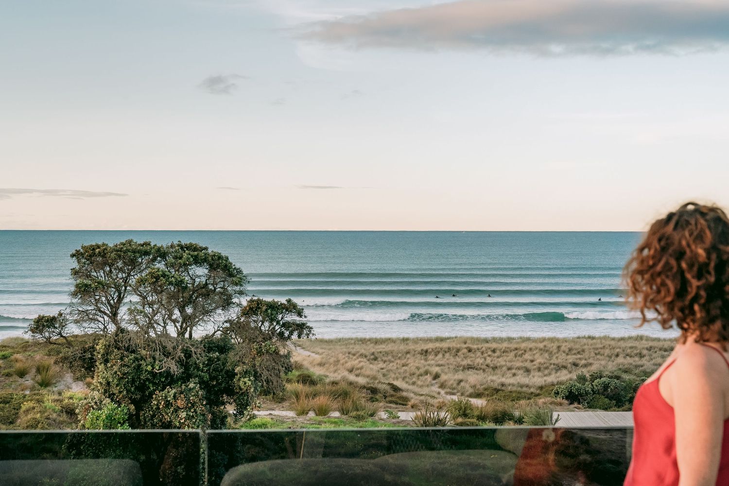 Scenic ocean view from a balcony with coastal vegetation and sandy beach in the distance.