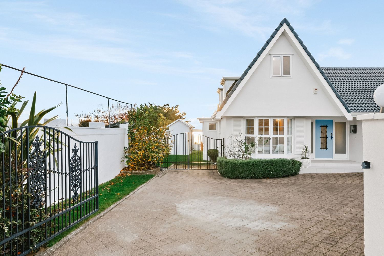 White coastal homes with paved driveway and decorative iron gates.