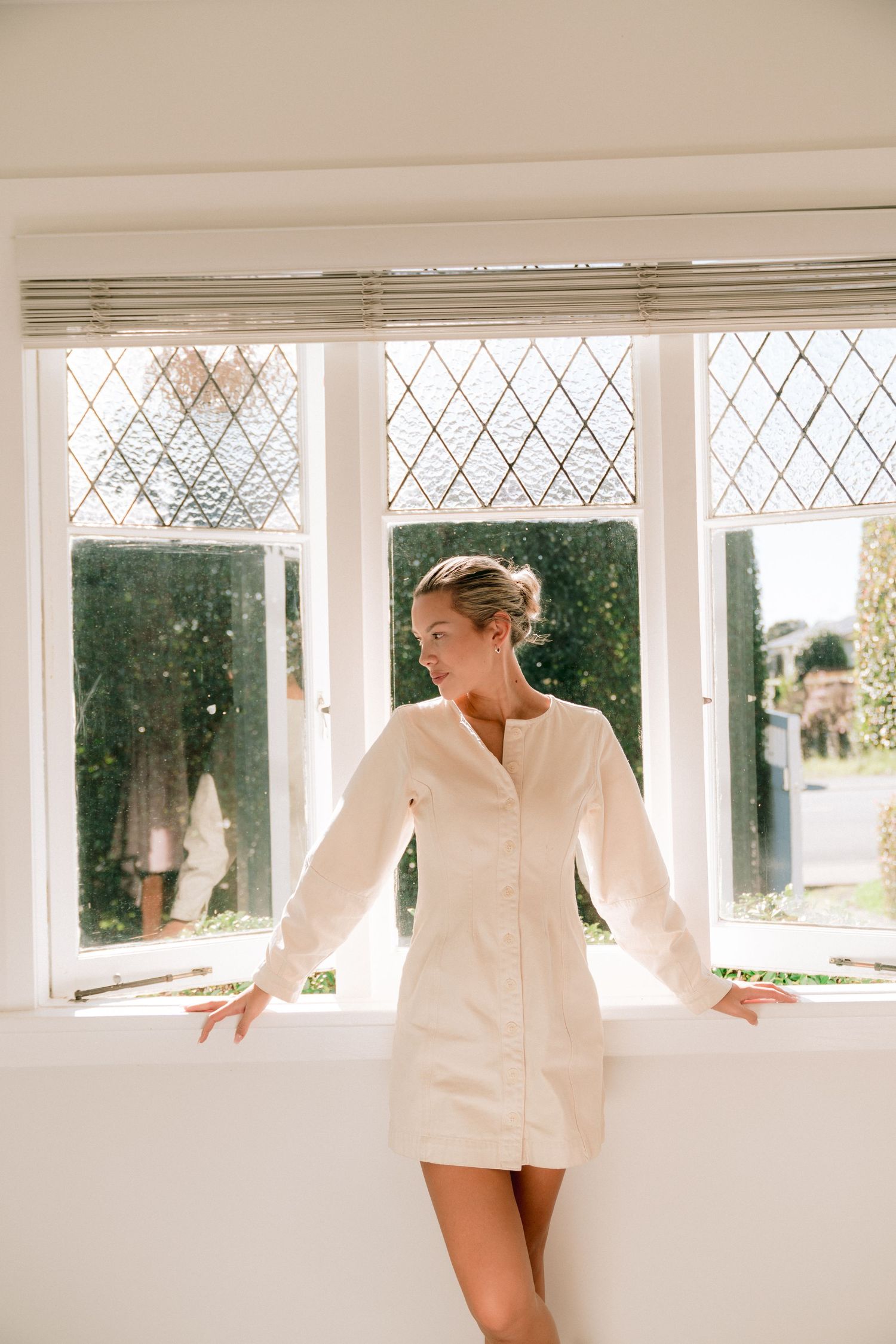 Someone in a white button-down shirt poses elegantly by a row of diamond-paned windows.