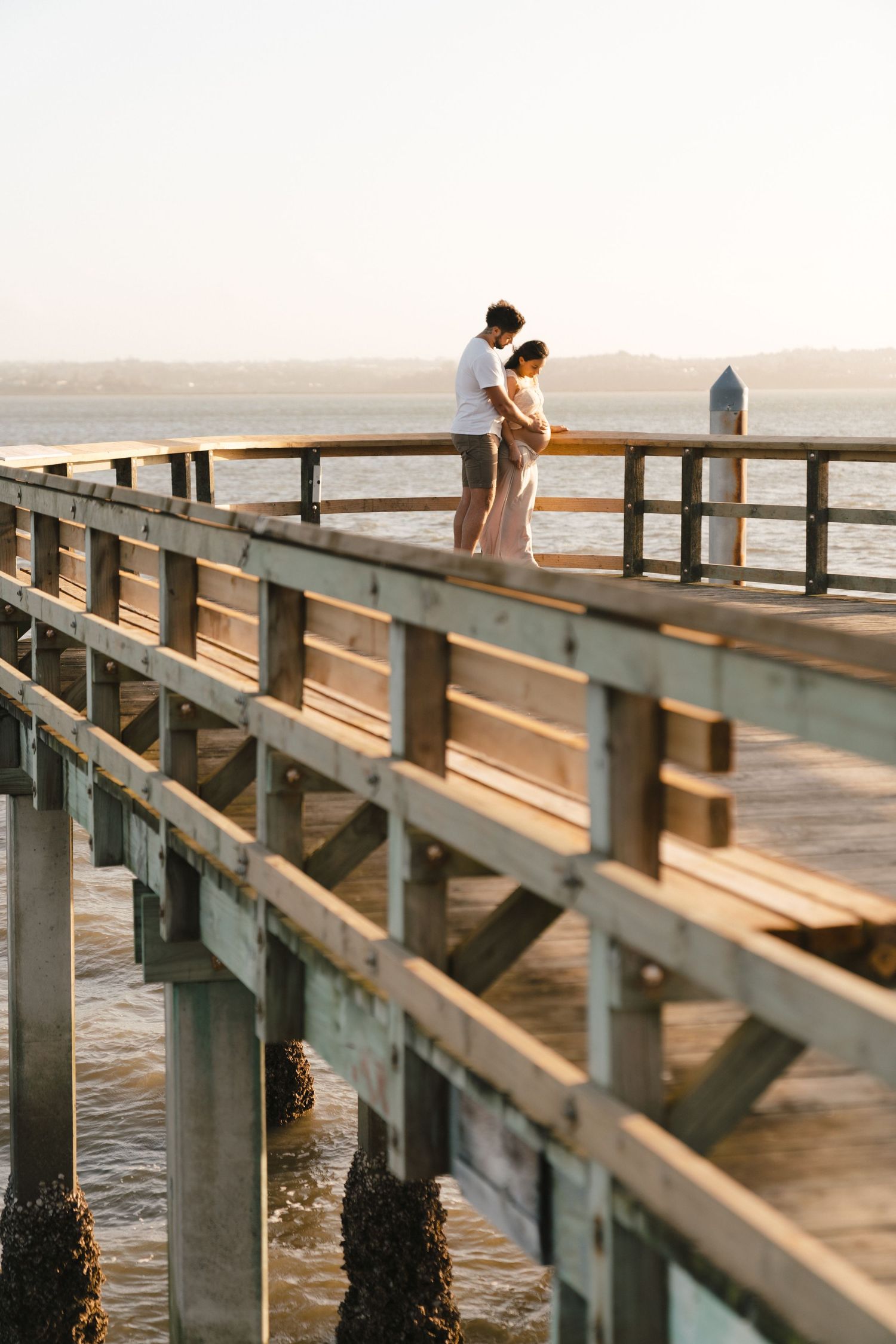 A scenic wooden pier stretches across calm waters at sunset, with figures creating silhouettes in the distance.