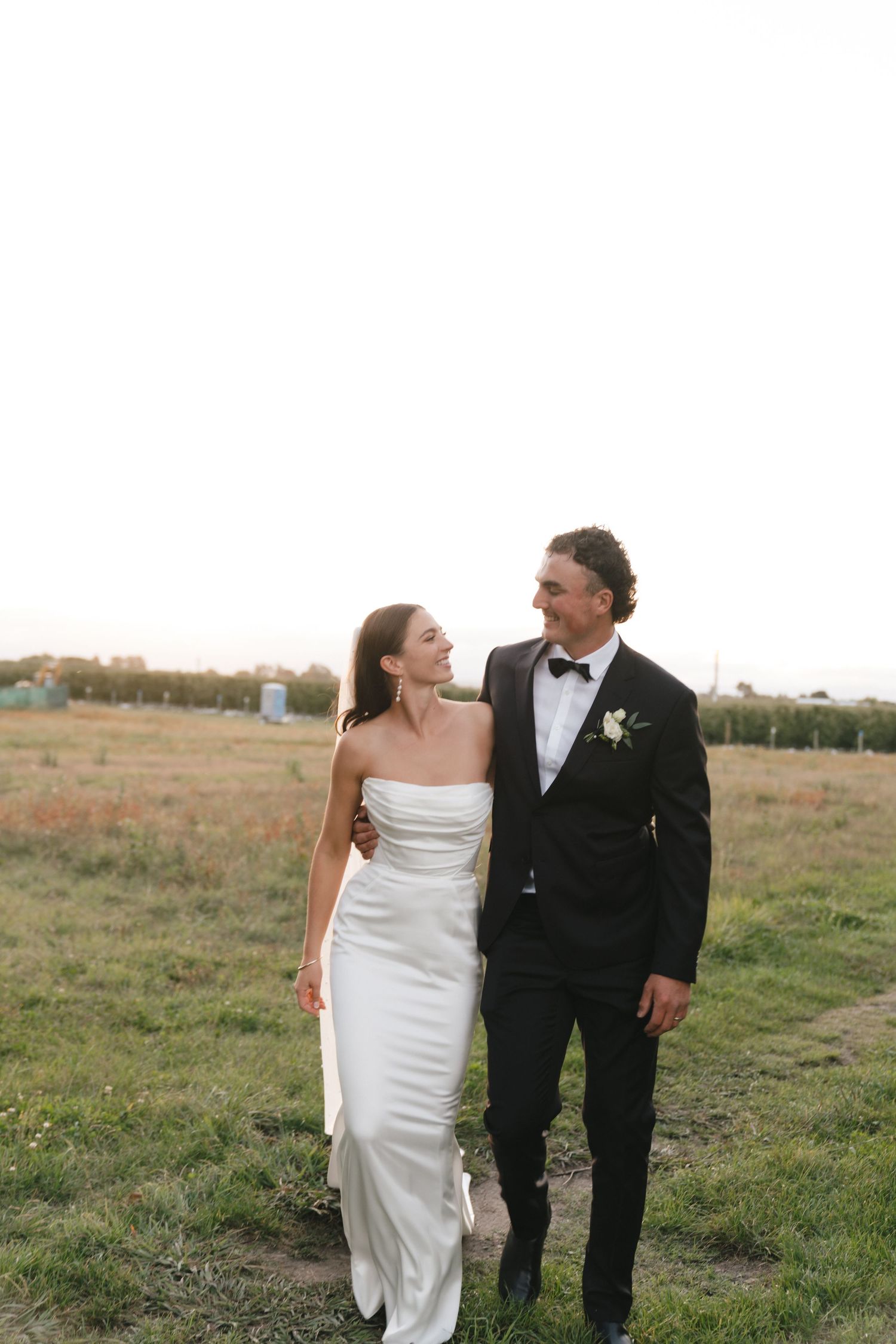 A bride and groom share an intimate moment while walking through a sunny field at sunset.