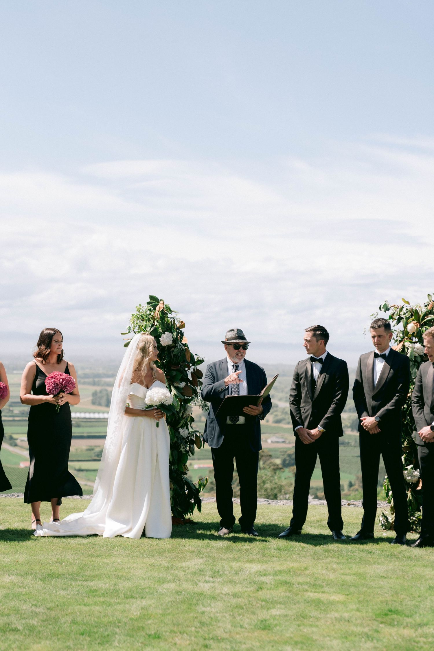 An outdoor wedding ceremony takes place on a hilltop with scenic mountain views in the background.