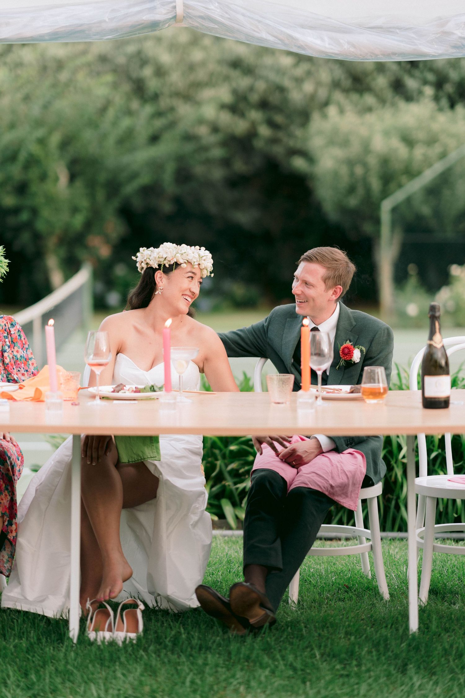 Casual outdoor wedding reception with couples dining at white tables.