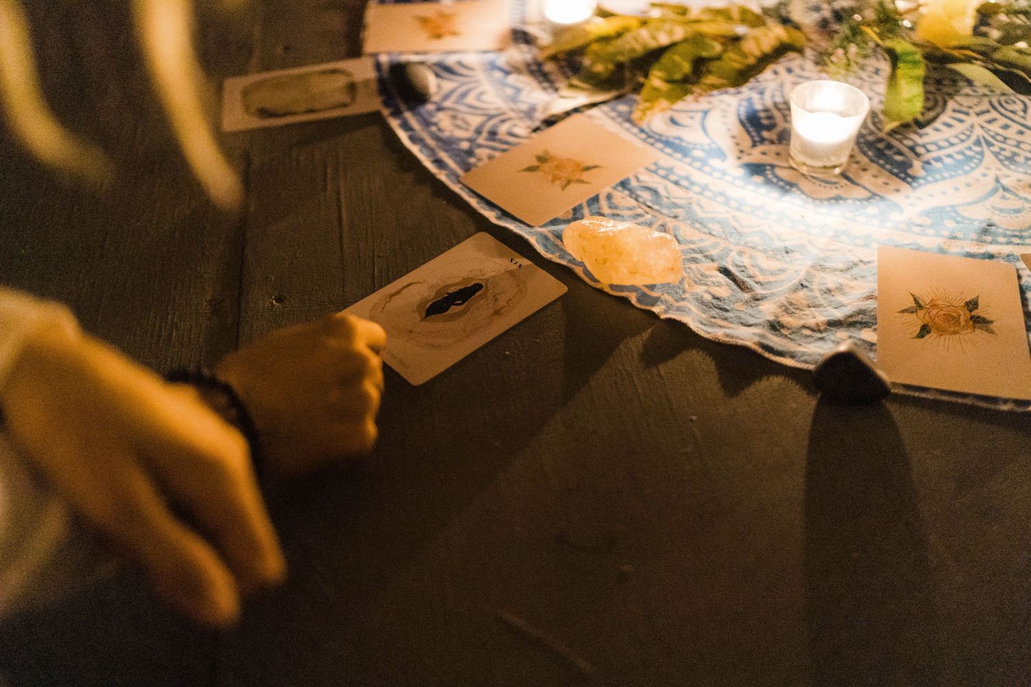 Hands holding cards at a dimly lit table with decorative flowers and candlelight.