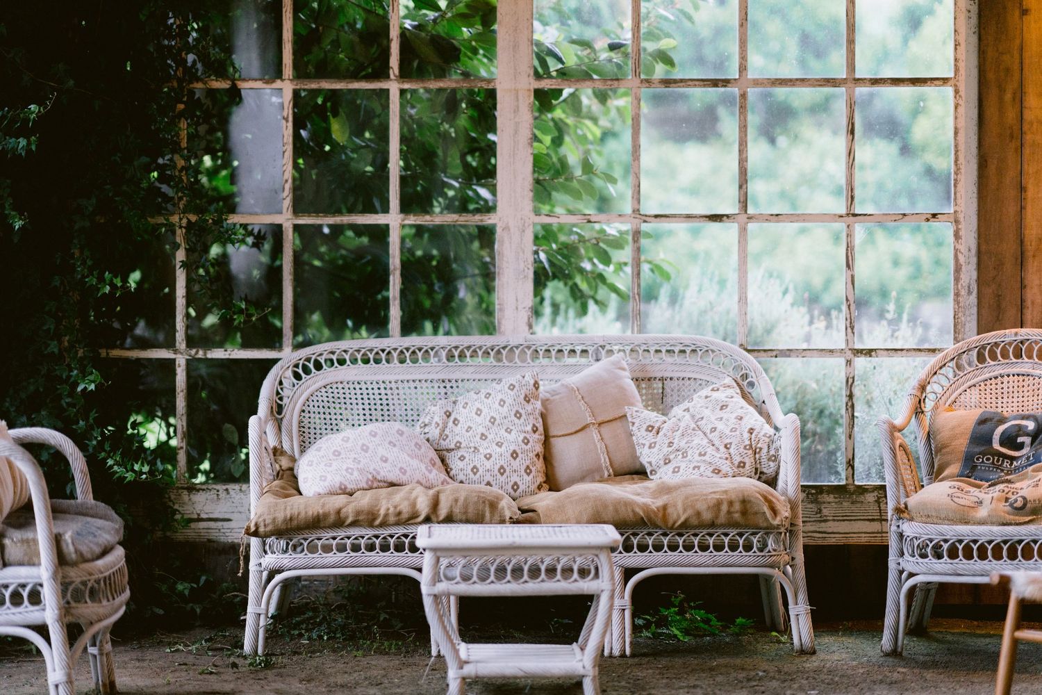 White wicker patio furniture with cozy cushions and pillows against a windowed backdrop.