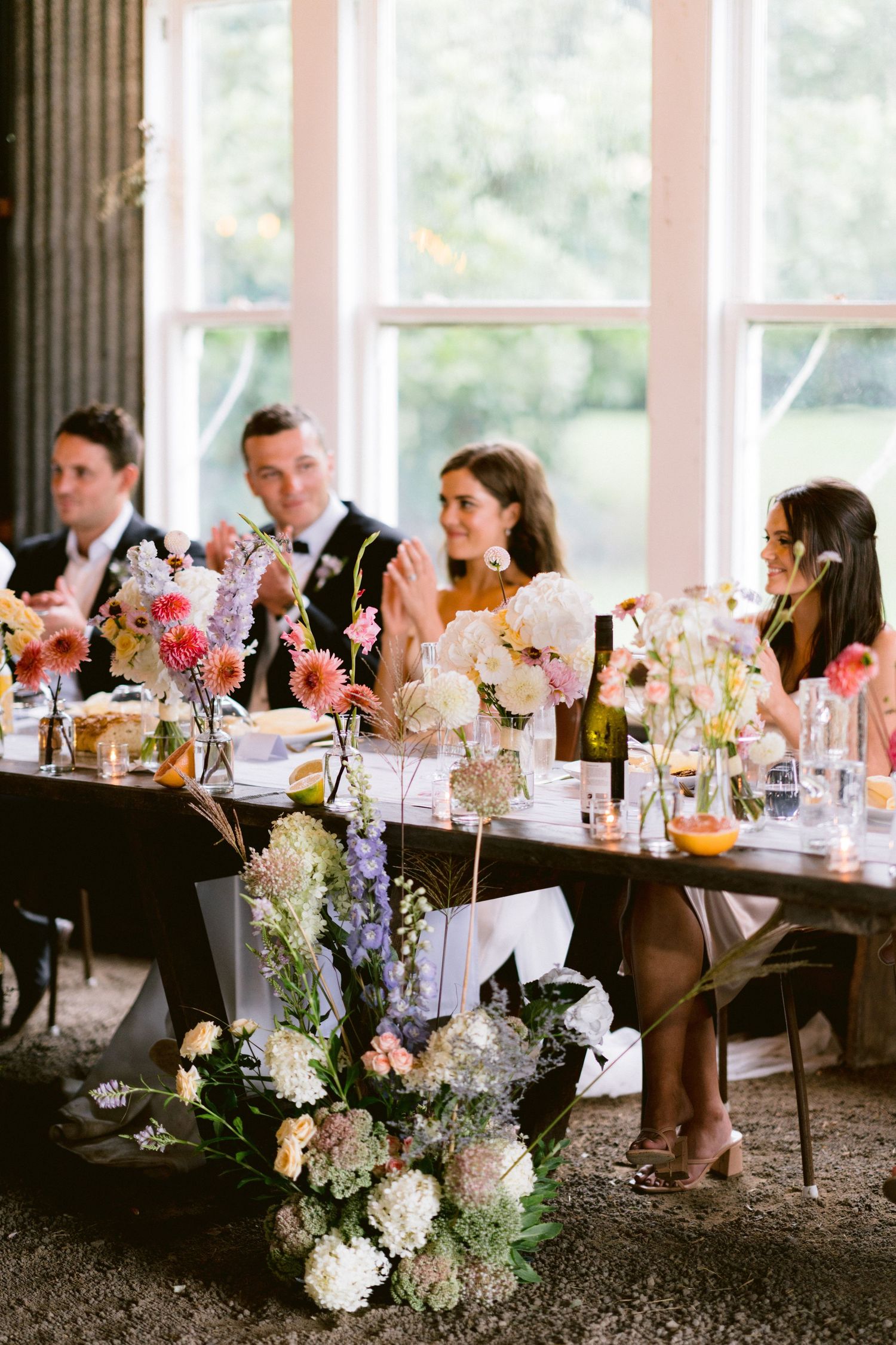 An elegant wedding reception table set with pink and purple floral arrangements and glassware.
