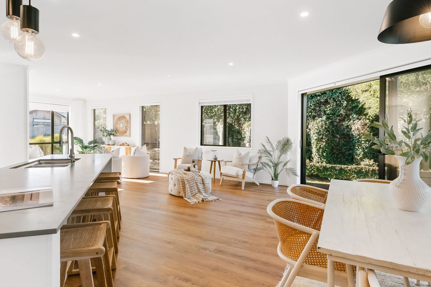 Modern open plan kitchen and dining area with wood floors, white walls, and natural light streaming through windows.