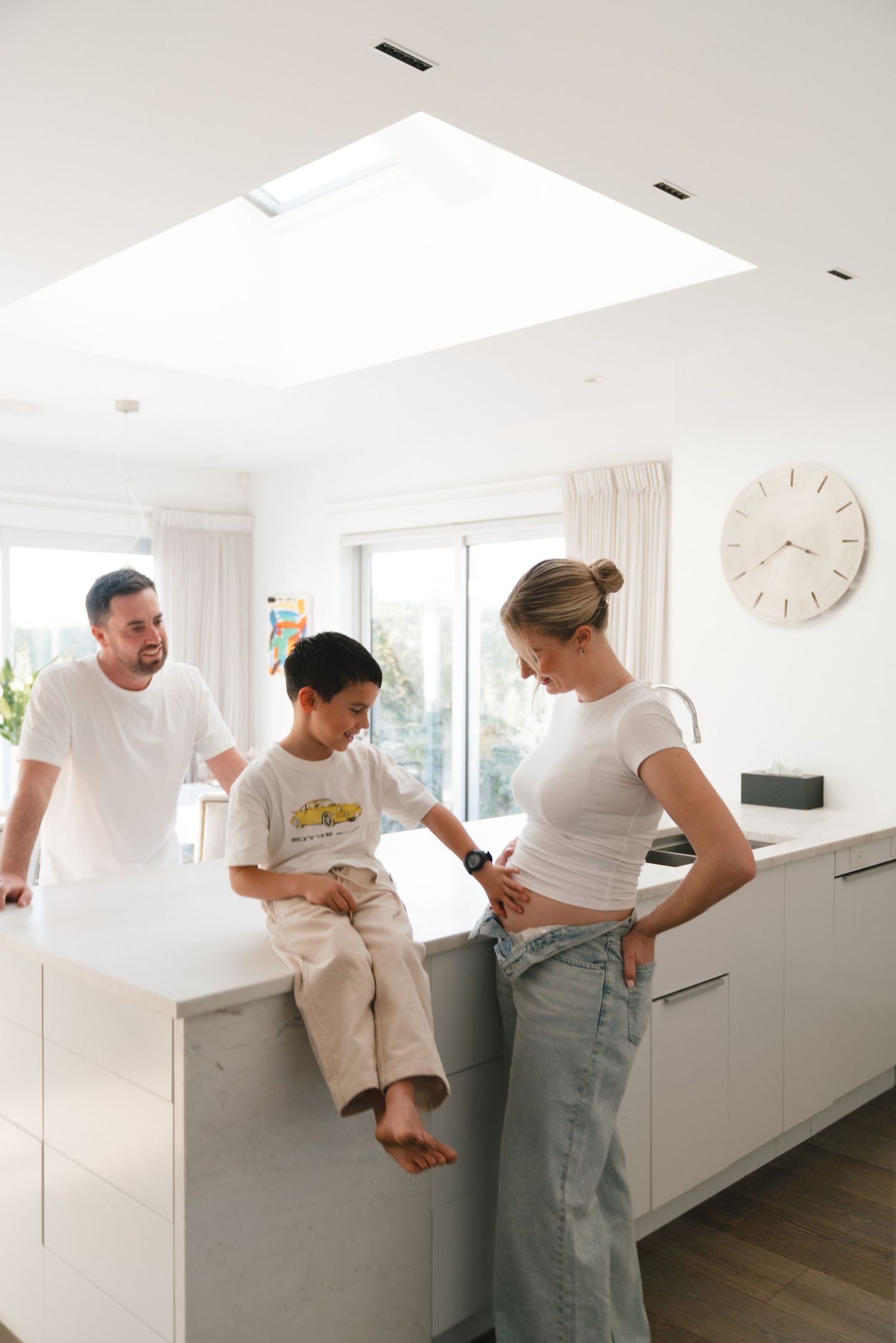 Family sharing a relaxed moment together in a modern white kitchen with skylight.
