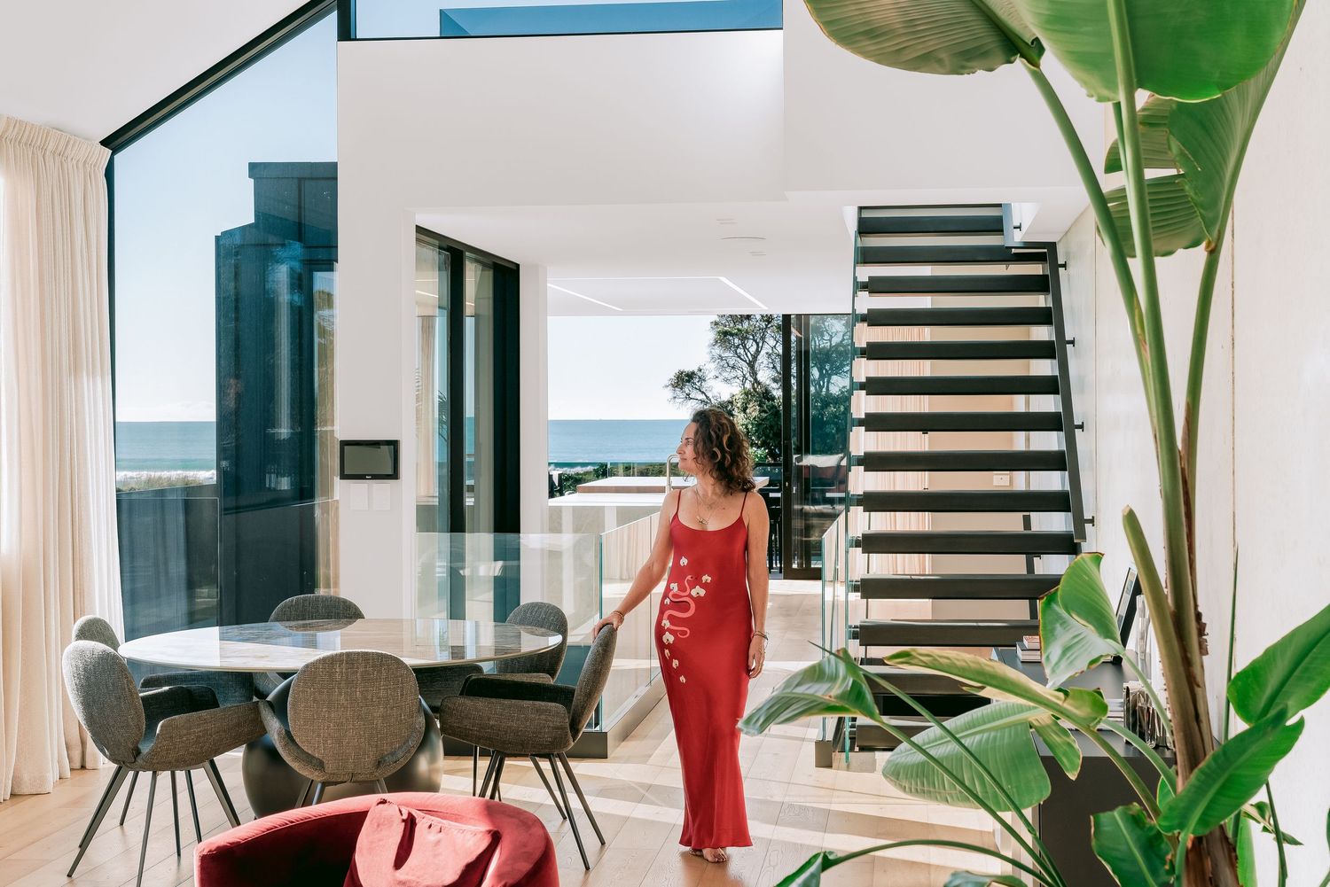 Contemporary living space with spiral staircase, indoor plants, and coastal views through large windows.