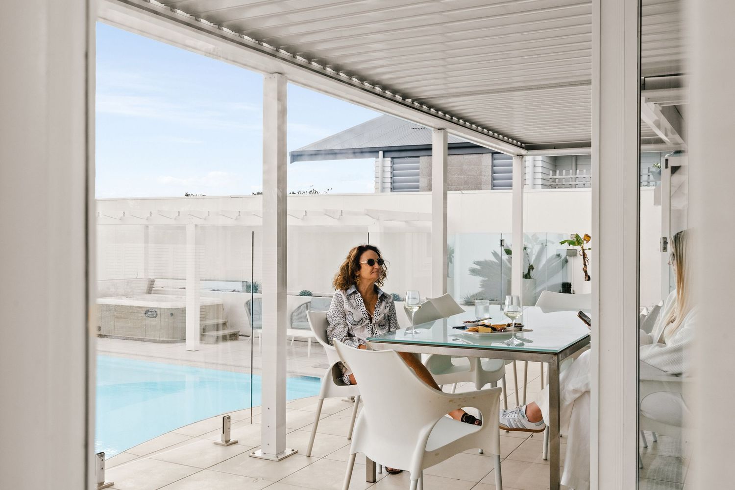 Outdoor dining setup next to swimming pool with modern white furniture.