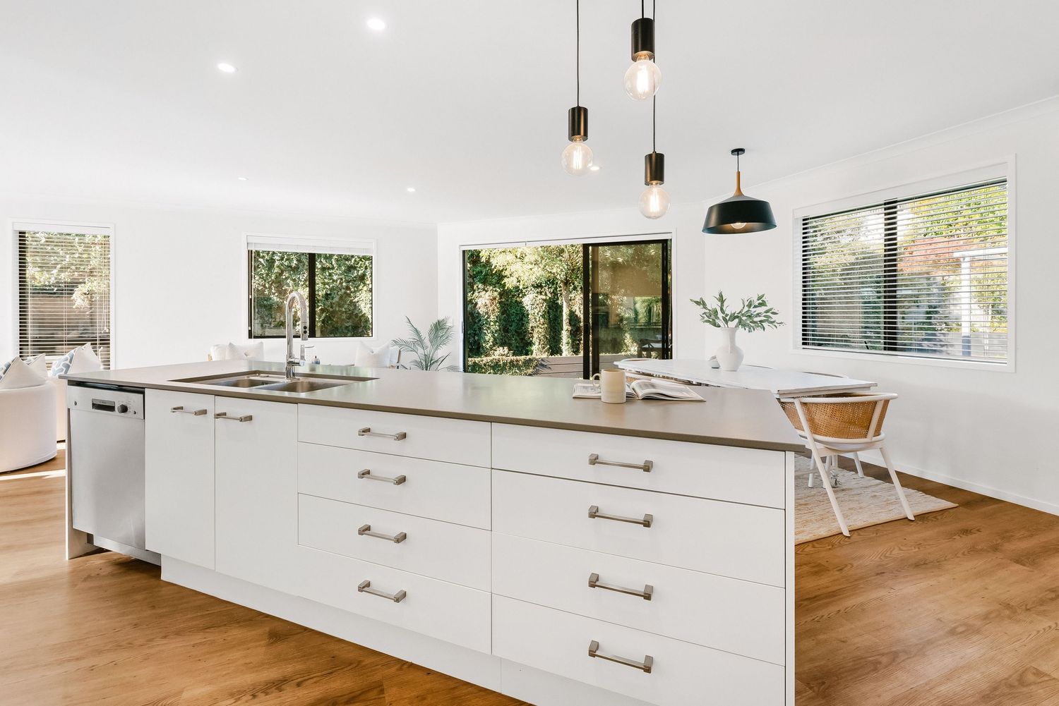 Modern white kitchen with large island, pendant lights, wood floors and multiple windows offering natural light.