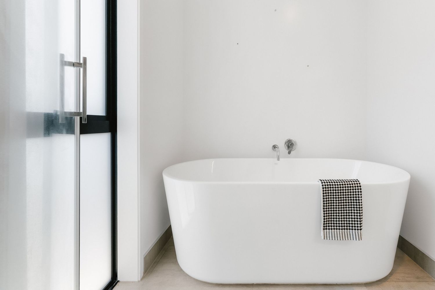 Modern freestanding white bathtub with gray towel in minimalist bathroom interior design.
