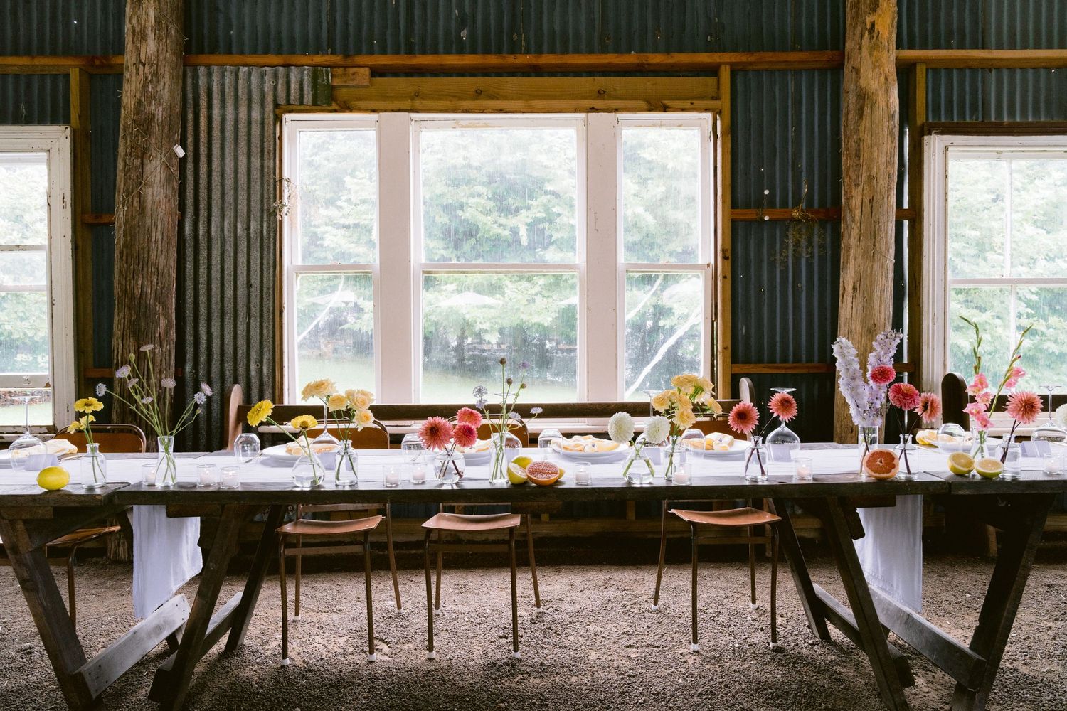 Long rustic wedding reception tables set inside a barn with large windows letting in natural light.