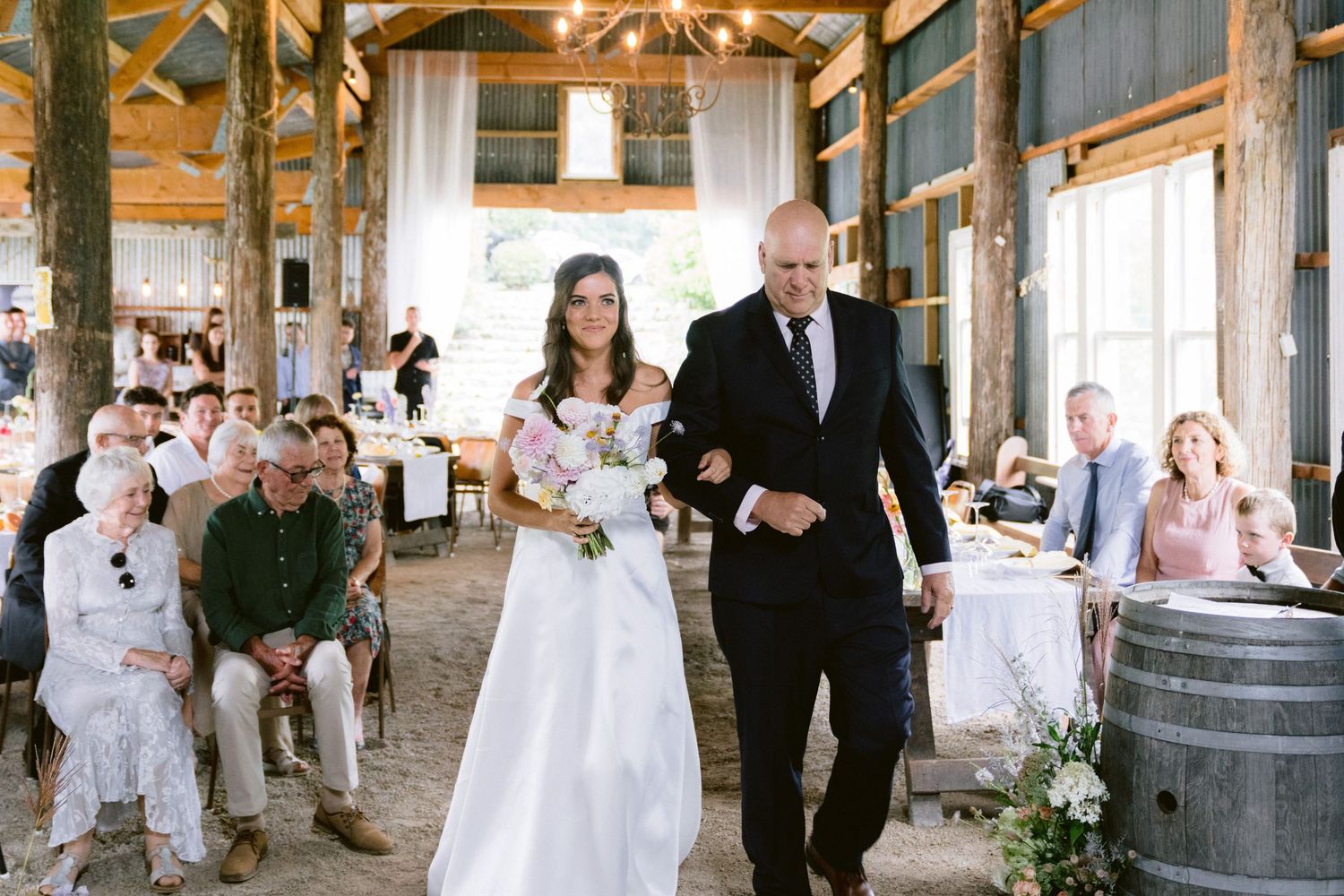 Wedding celebration inside a rustic barn venue with exposed wooden beams and white draping.