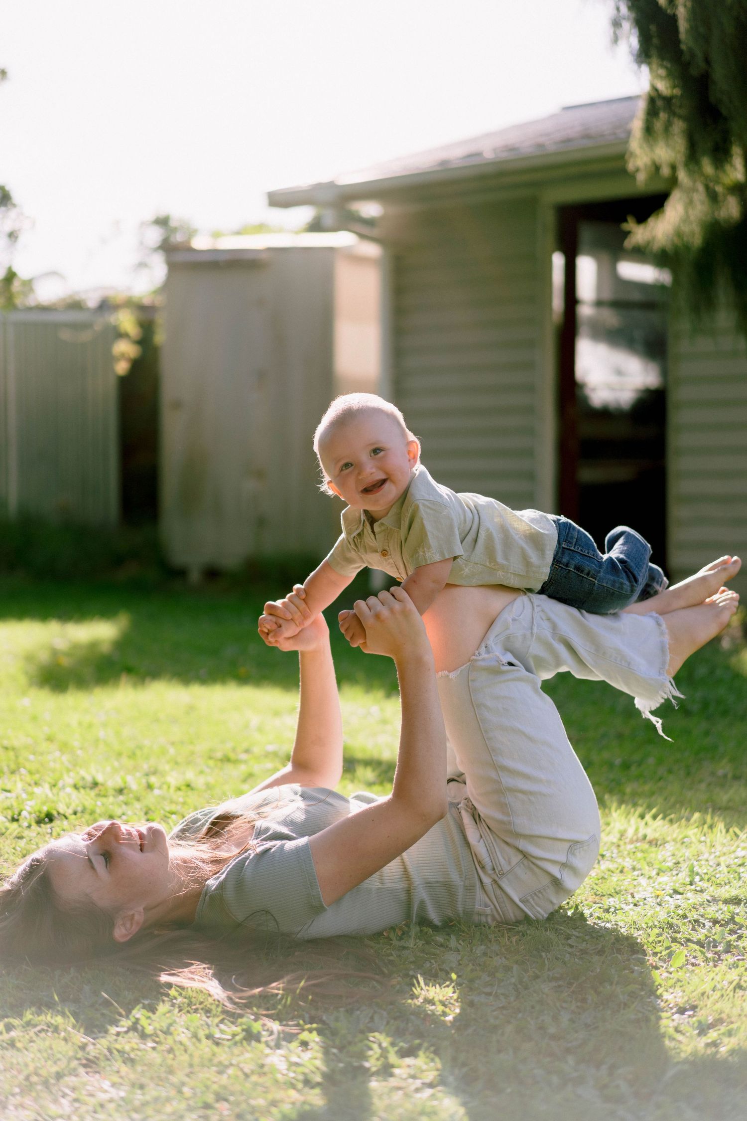 A heartwarming moment of parent and child playing together on the grass in a sunny backyard setting.