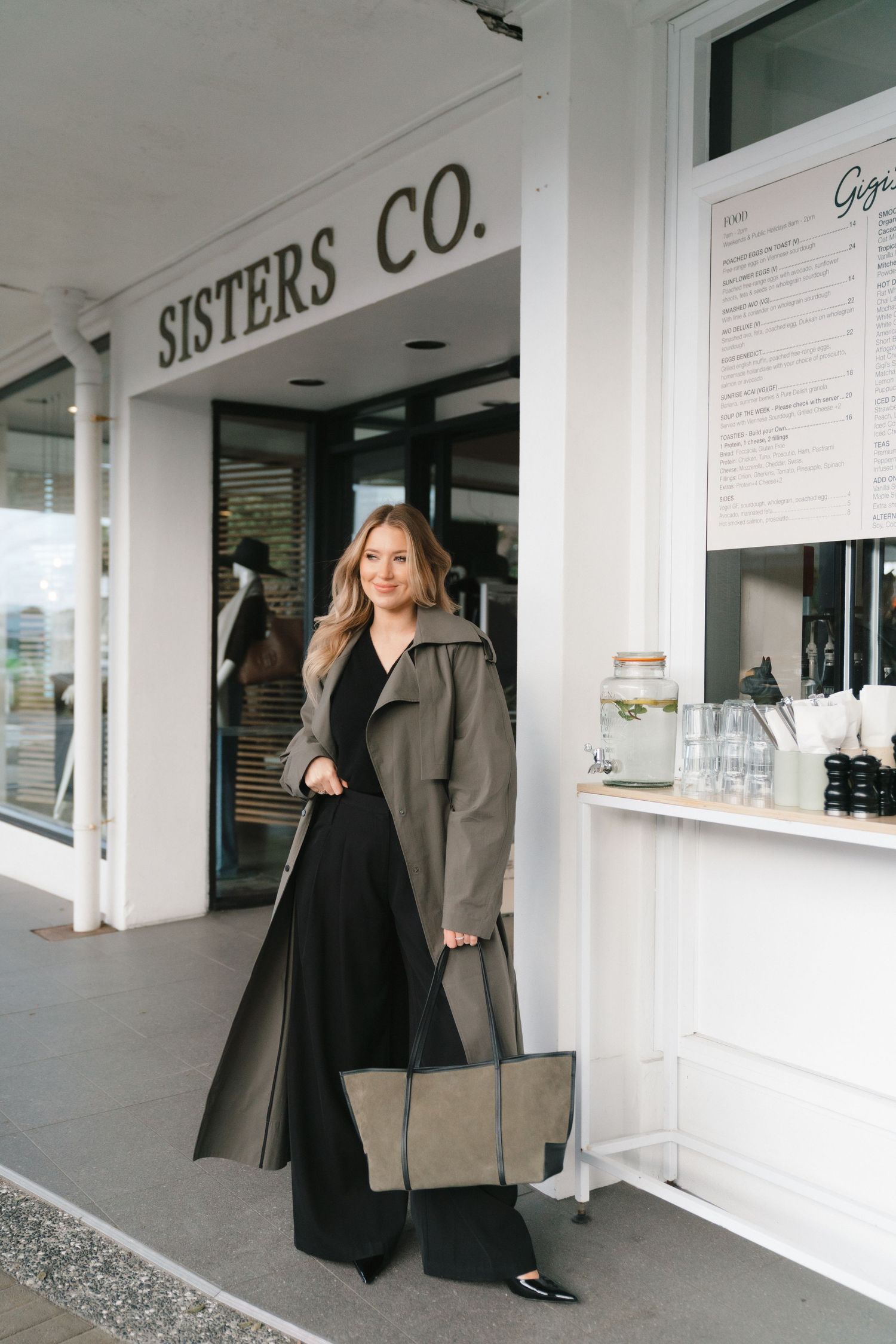Fashion retail storefront with white exterior showing clothing display and service window at Sisters Co. shop.