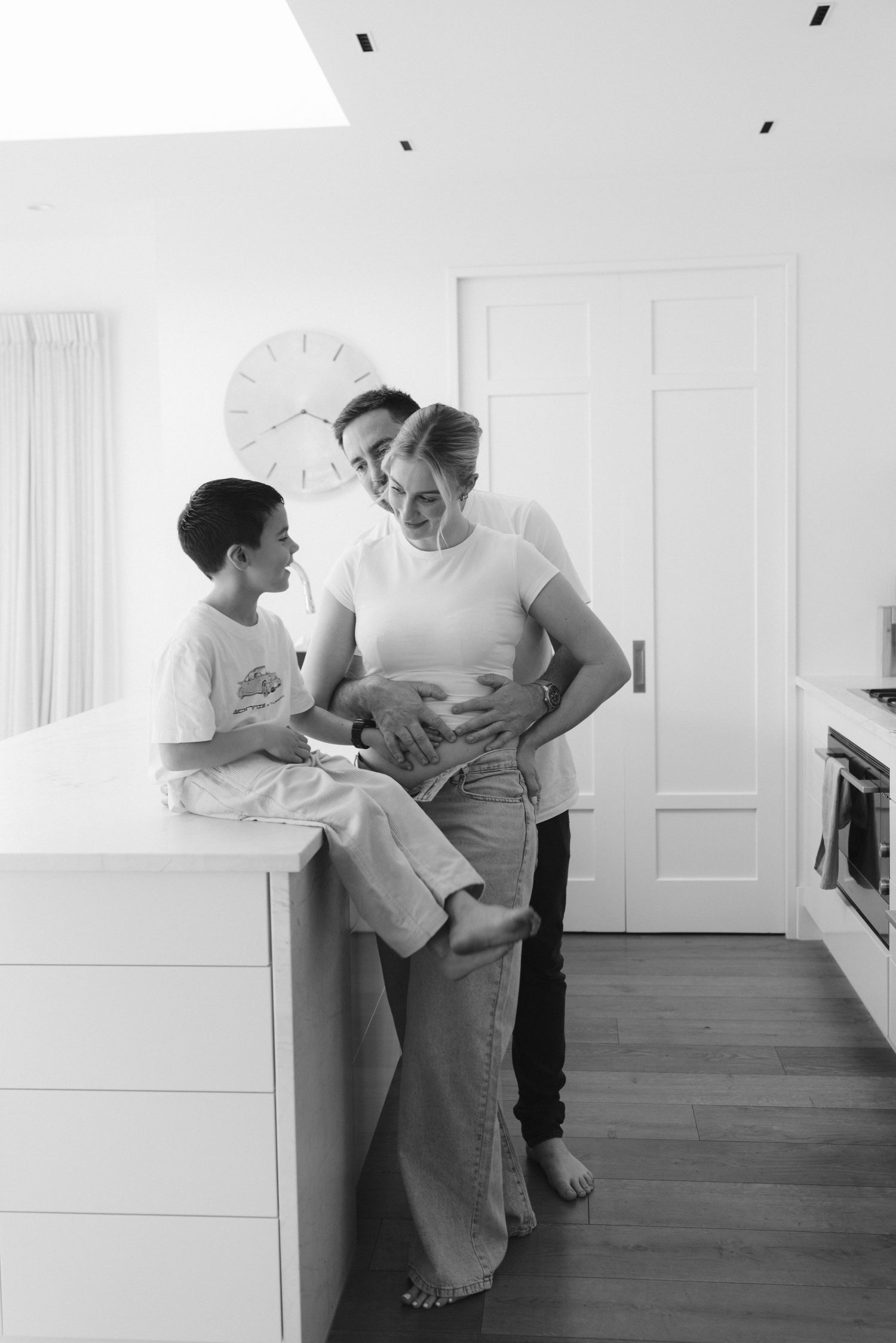 A tender moment shared in a bright modern kitchen with white cabinets and wood flooring.