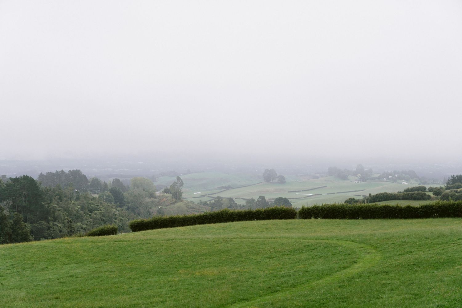 Rolling green hills and fields fade into a misty countryside landscape with hedgerows and trees.