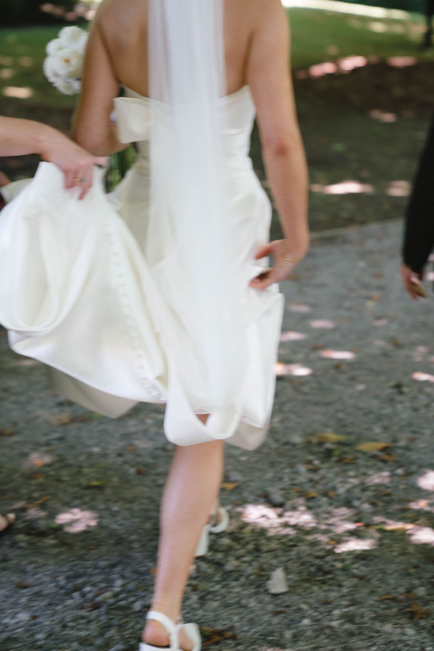 Cropped view of a white wedding dress flowing in motion on a sunlit garden path.