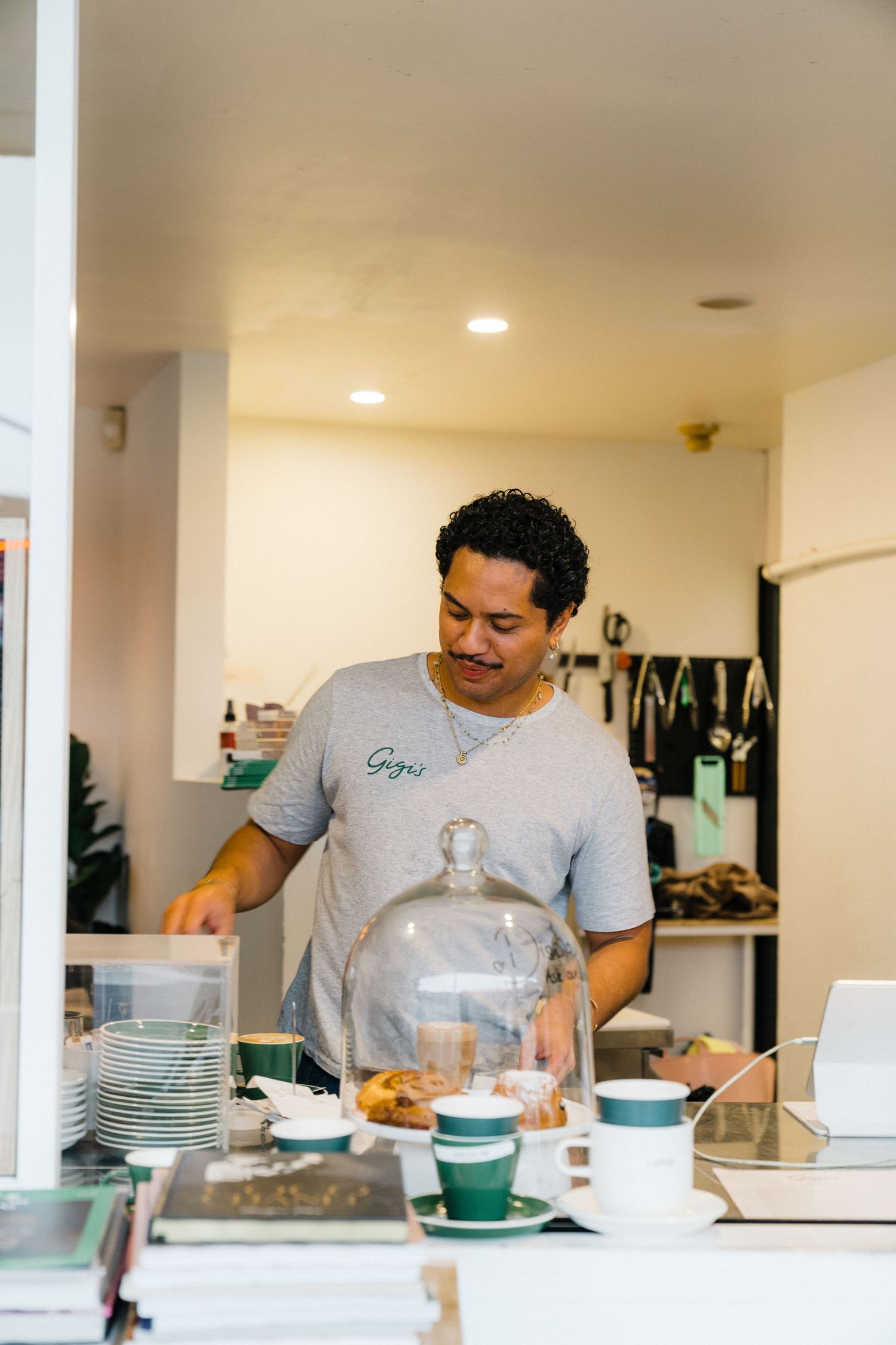 People preparing food and drinks in modern cafe kitchen with turquoise cups and white plates on counter.