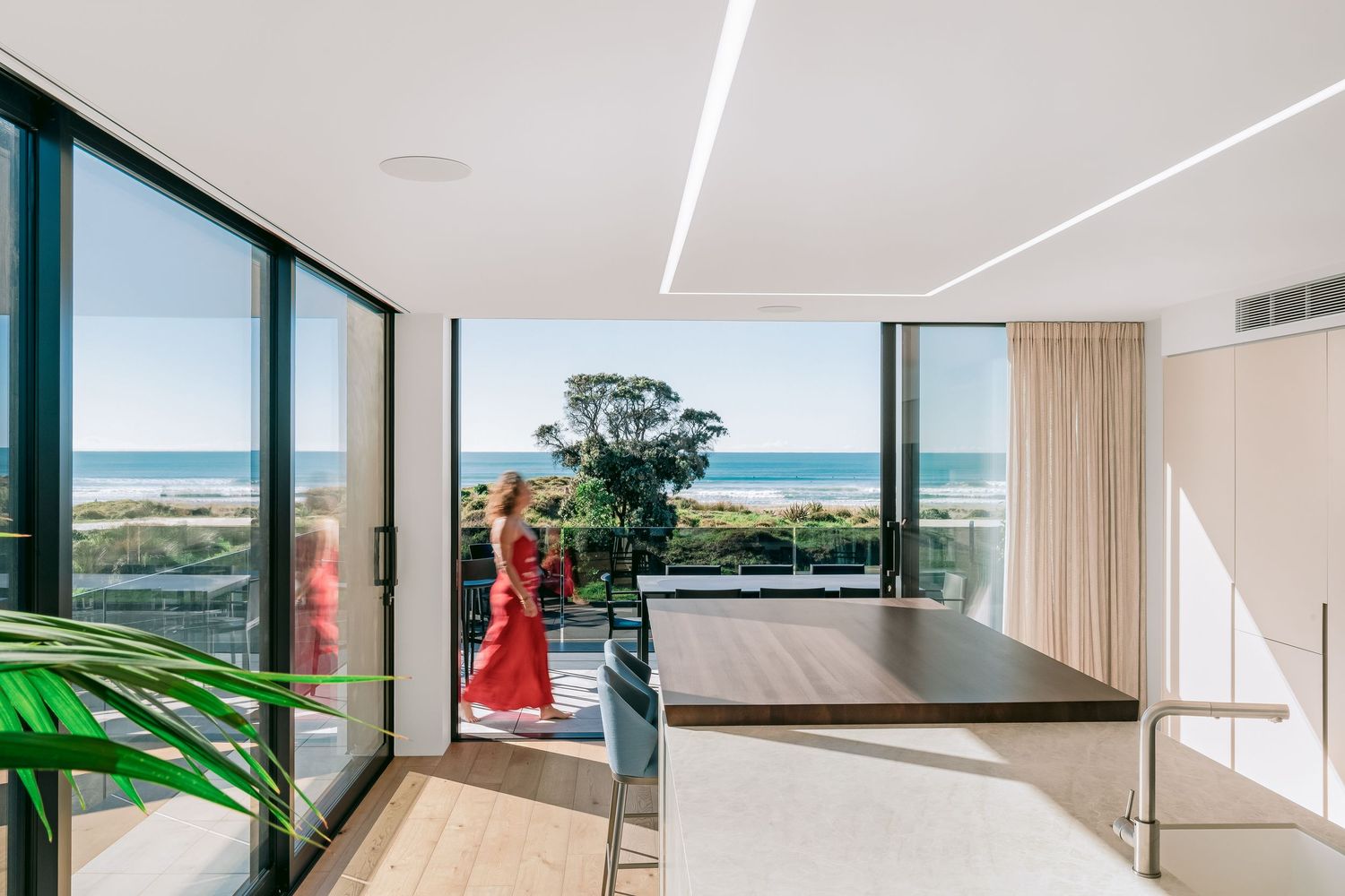 Panoramic view of an open-concept modern home interior with glass walls showcasing coastal scenery.