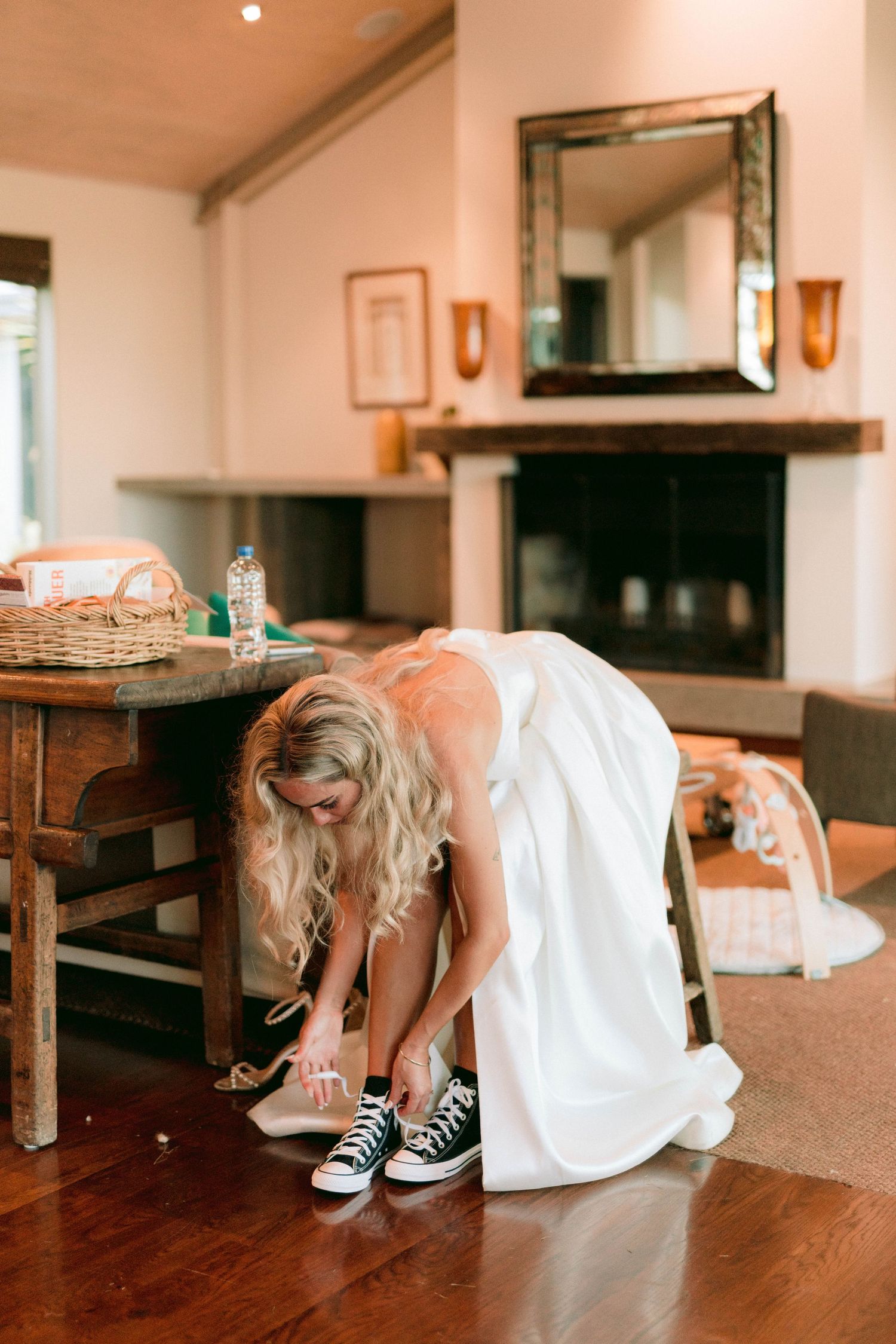 A person in a white dress looks underneath dark wooden furniture in what appears to be a dining room.