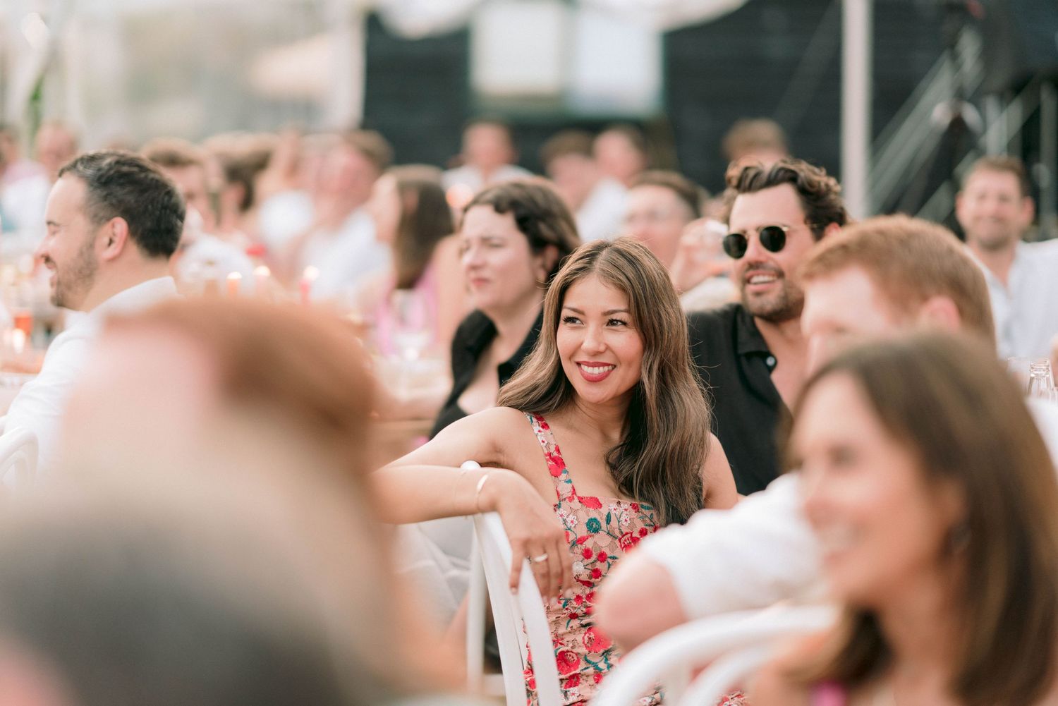 Wedding guests seated outdoors enjoying sunny celebration in garden setting.