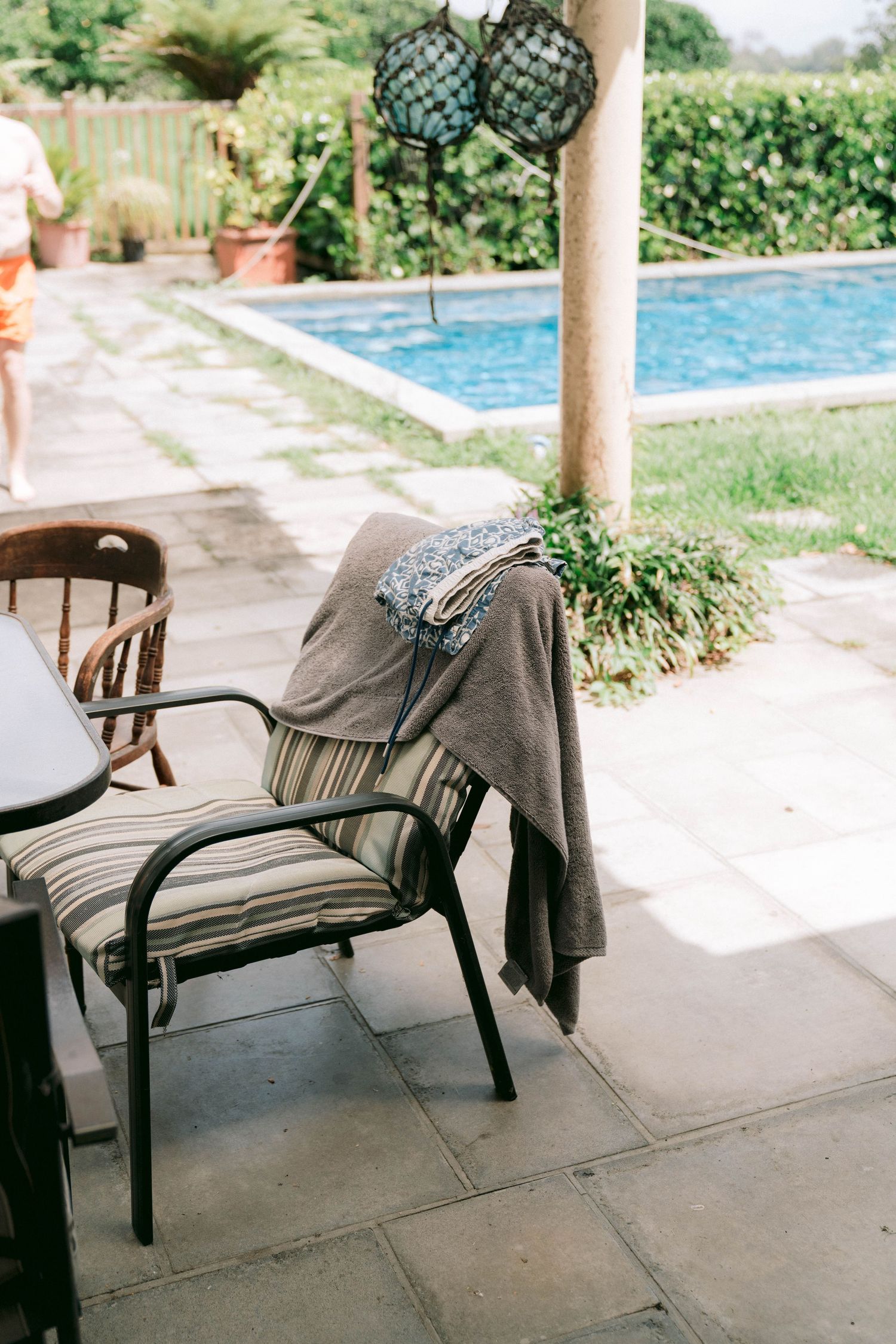 A poolside patio scene with an empty chair and decorative hanging lanterns in a tropical garden setting.
