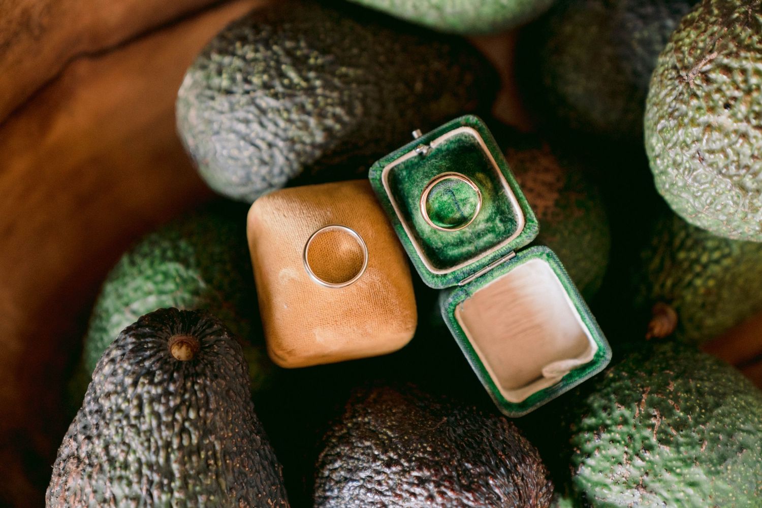Wedding rings displayed in green and coral colored ring boxes surrounded by textured fabric.