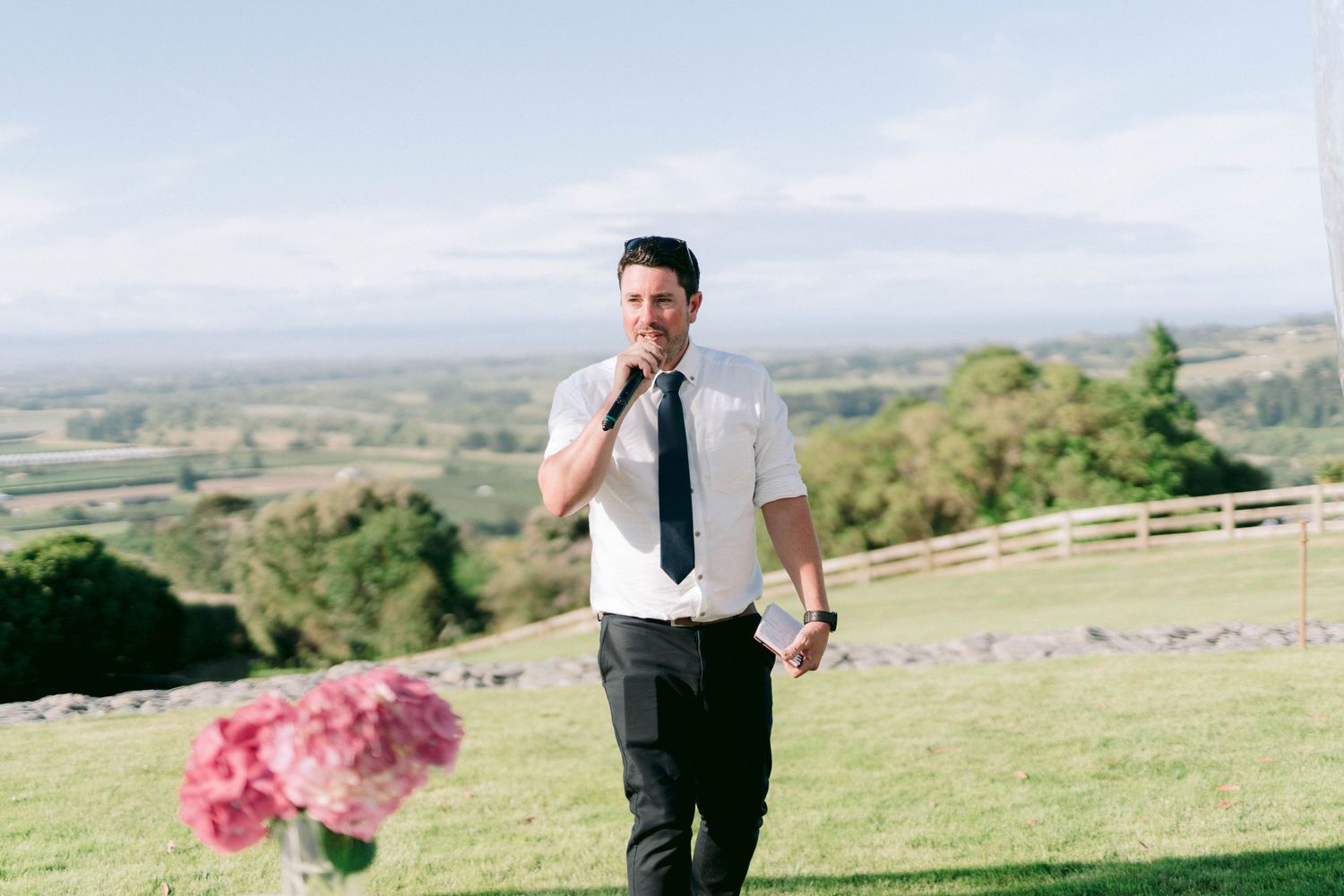 Person in formal attire walking across grassy hillside with mountain backdrop.