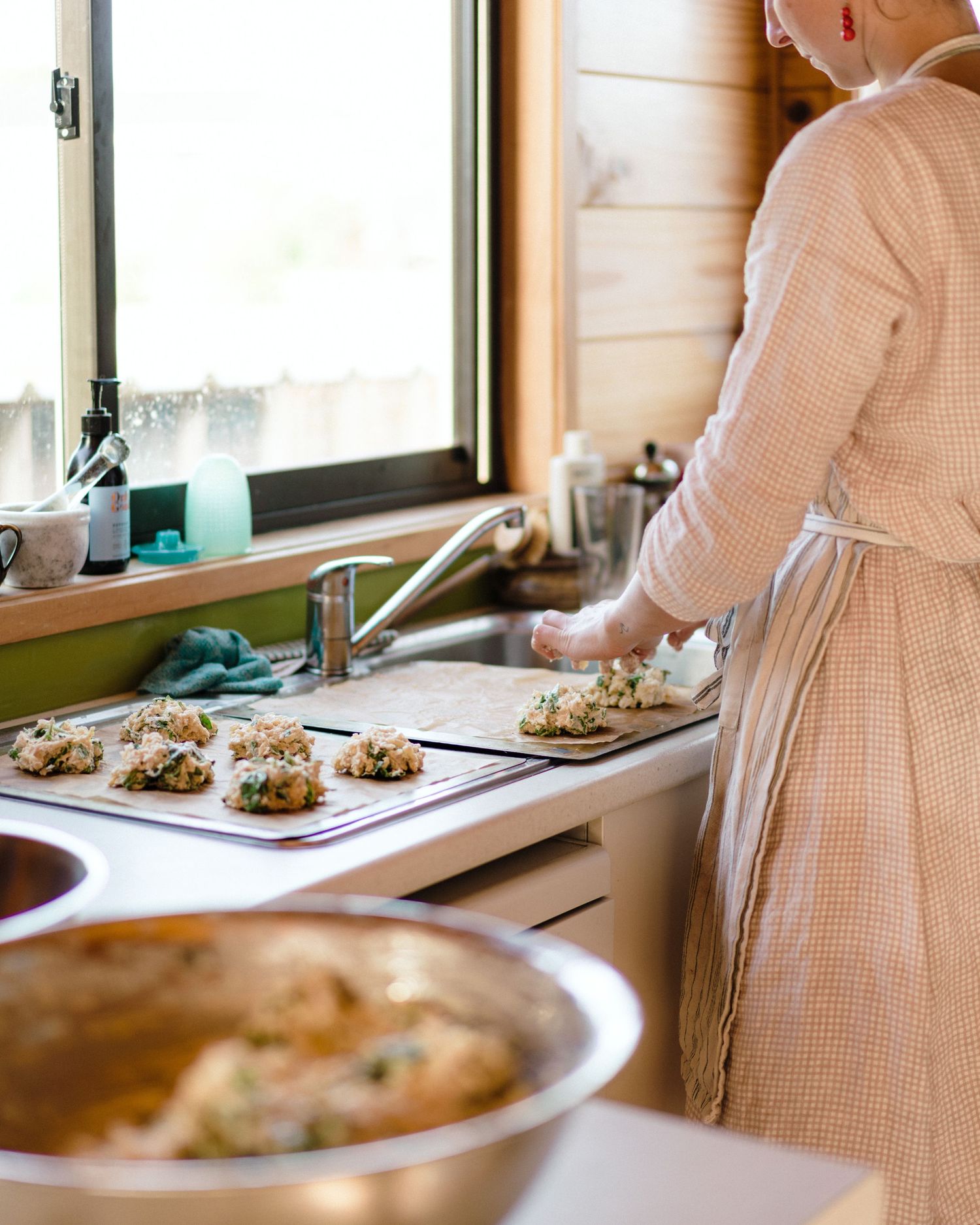 Someone in a checkered dress prepares variations of stuffed mushrooms on a kitchen counter for a food service event.