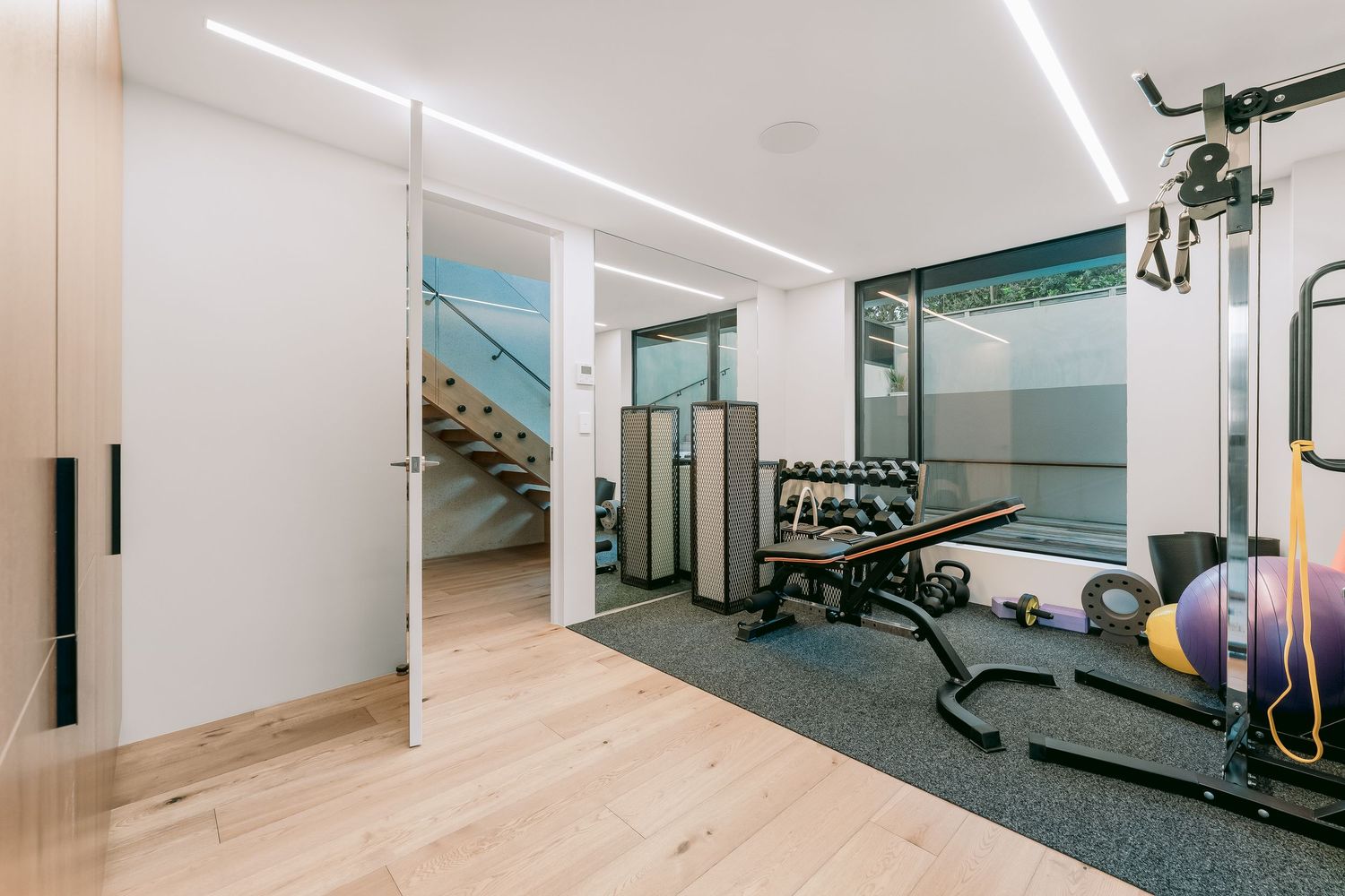 Spacious fitness room with exercise machines, light wood flooring, and recessed LED lighting.