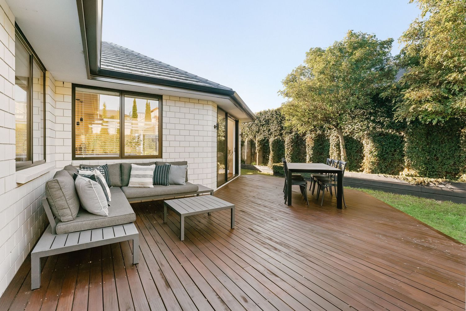 Long wooden deck extending along the side of a modern house with glass sliding doors.
