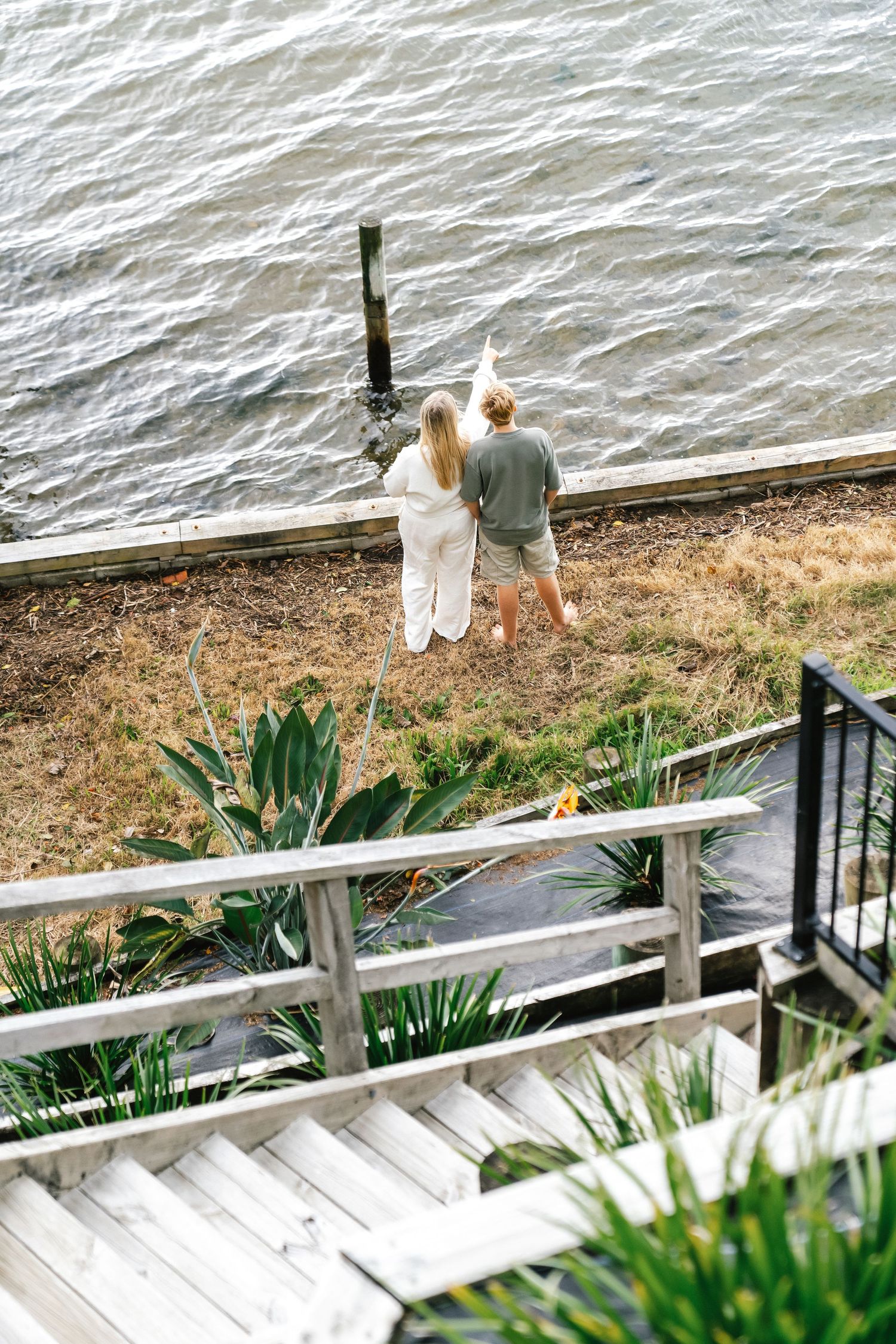Scenic waterfront deck with white railings and tropical plants overlooking calm waters.