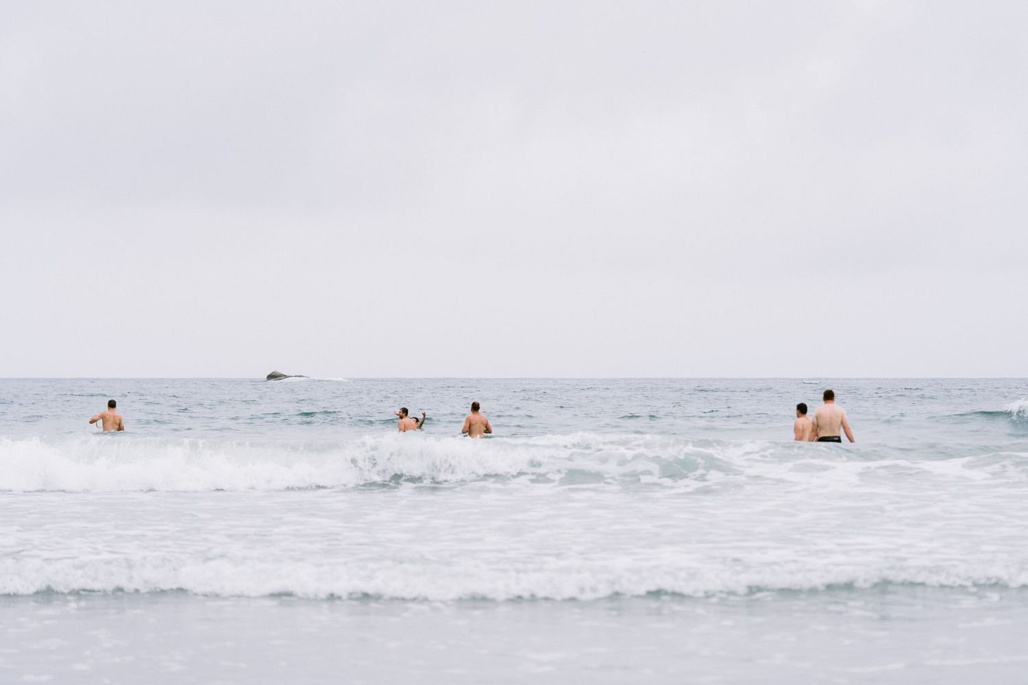 Several people swimming and playing in ocean waves on a misty summer day at the beach.