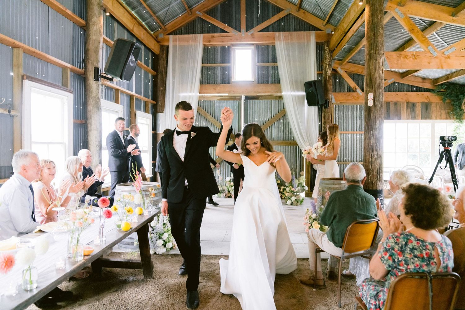 Panoramic view of a barn wedding reception with rustic wood beams and natural lighting.