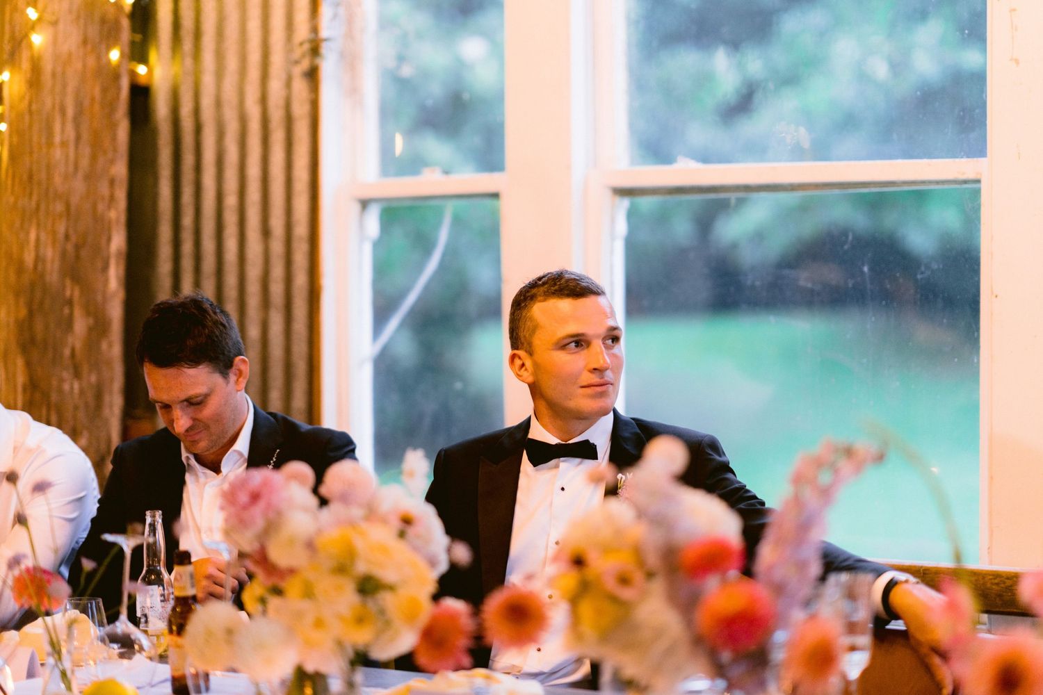 Reception tables decorated with colorful floral centerpieces in a sunlit room with floor-to-ceiling windows.