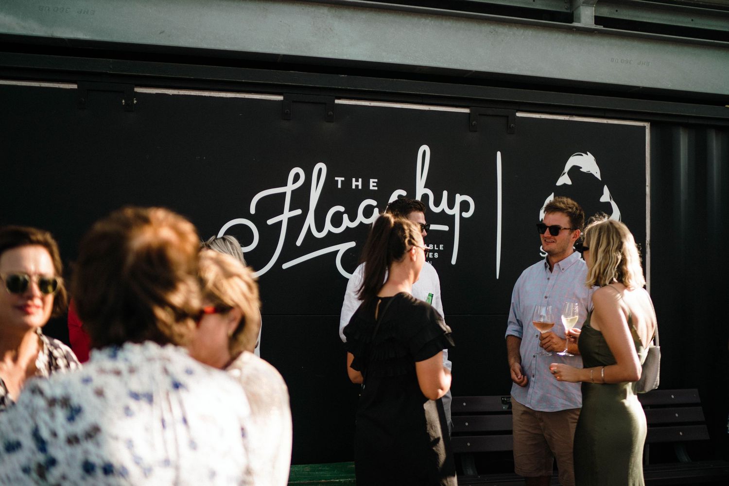 Customers gather outside The Float Up coffee shop with neon signage during a sunny afternoon.