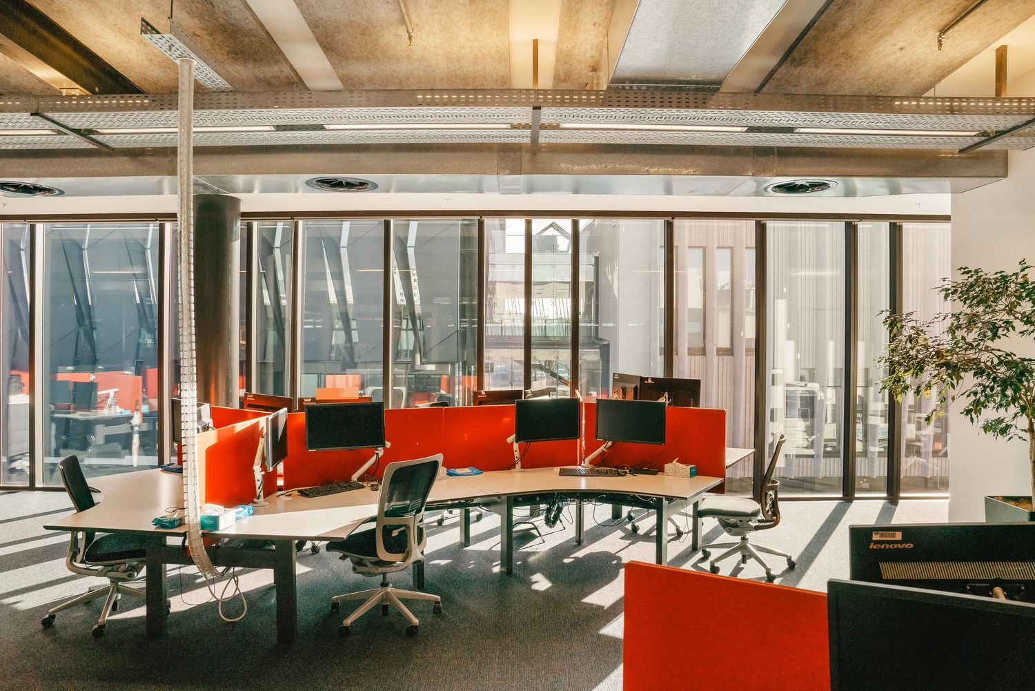 Contemporary office interior featuring glass walls, orange lounge chairs, and sleek industrial design elements.