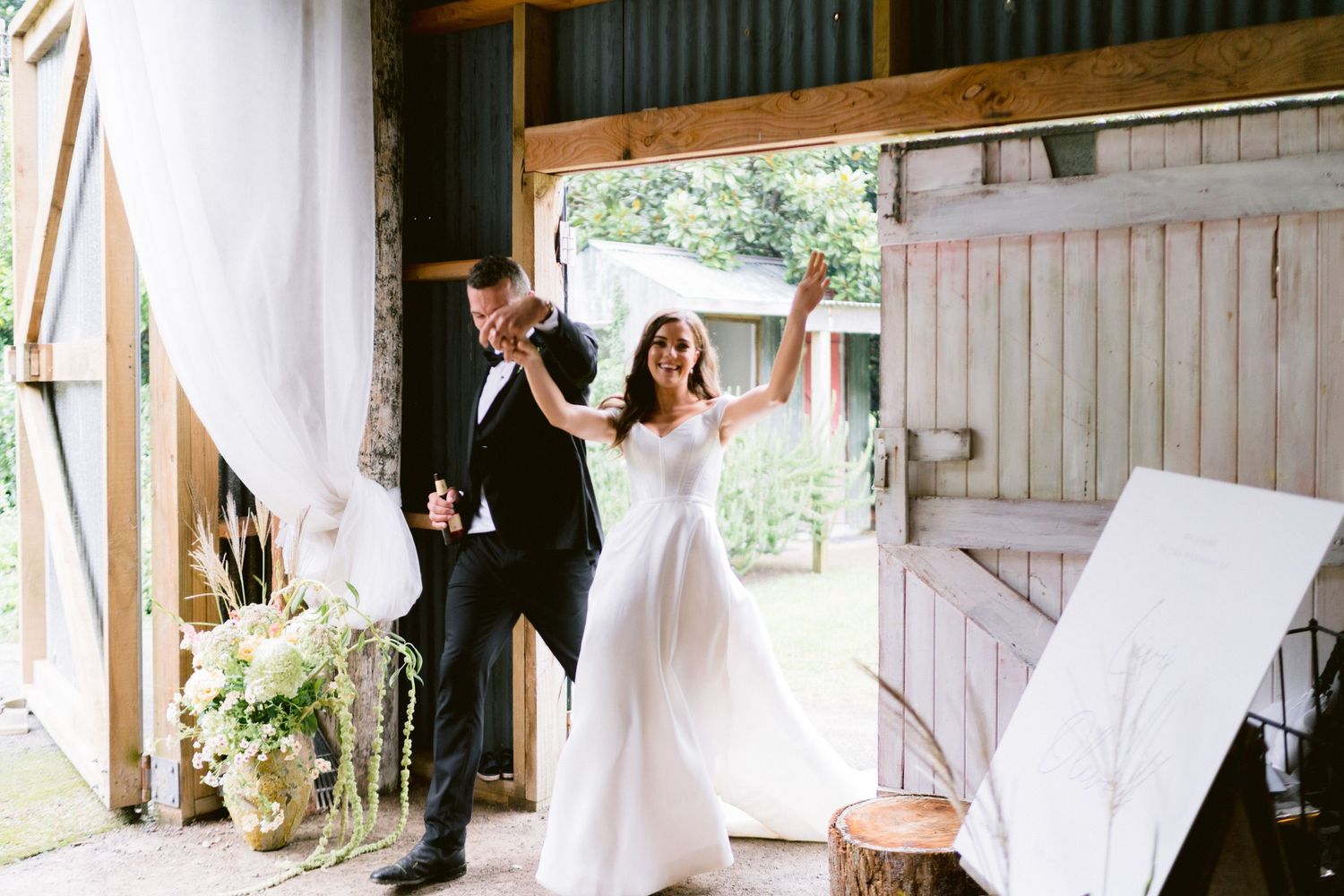 Wedding celebration inside a rustic barn with white curtains and wooden details.
