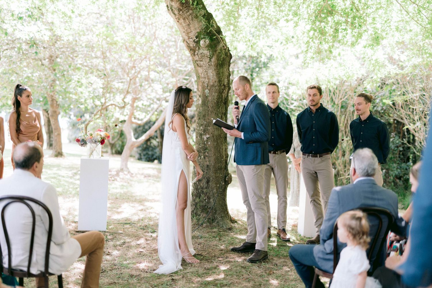 An intimate outdoor wedding ceremony taking place under tall trees.