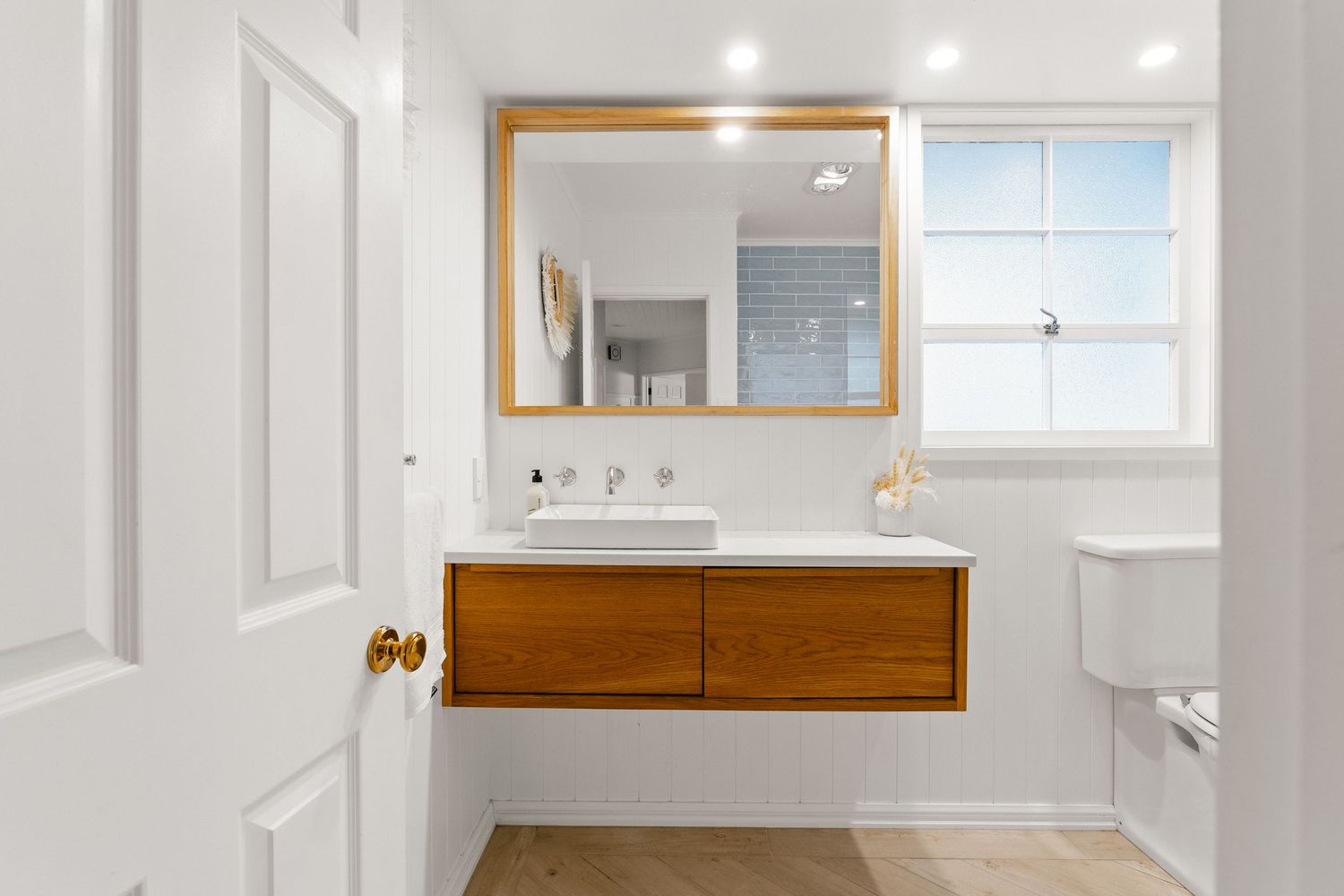Modern bathroom featuring floating wood vanity, large mirror, and clean white fixtures.