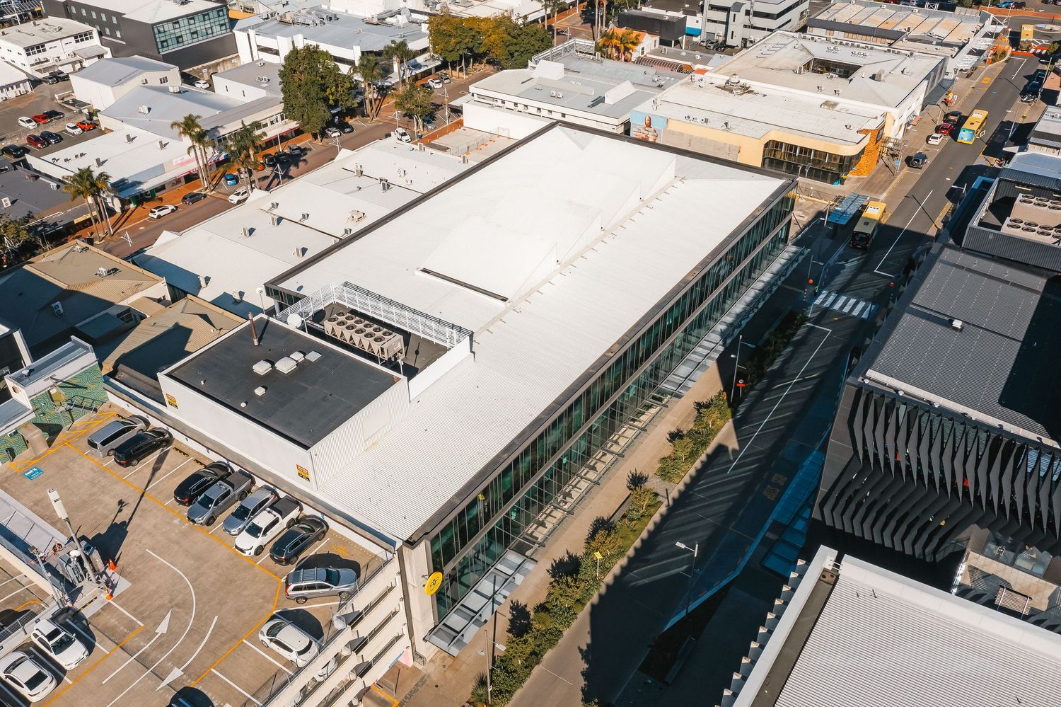 Aerial view of industrial buildings with white rooftops and loading docks seen from above in an urban area.