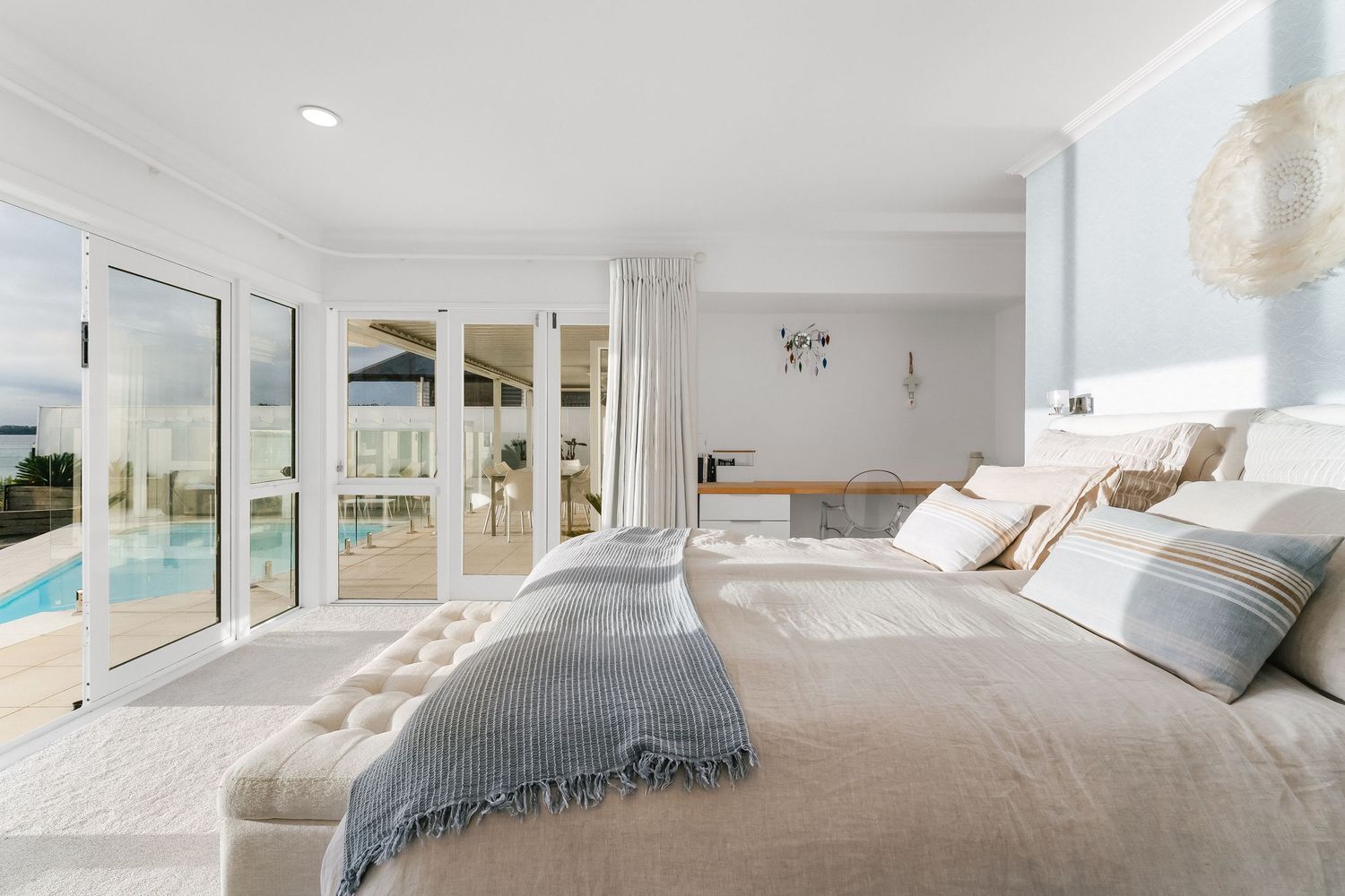 Modern coastal home bedroom featuring white linens, natural light, and panoramic ocean views.