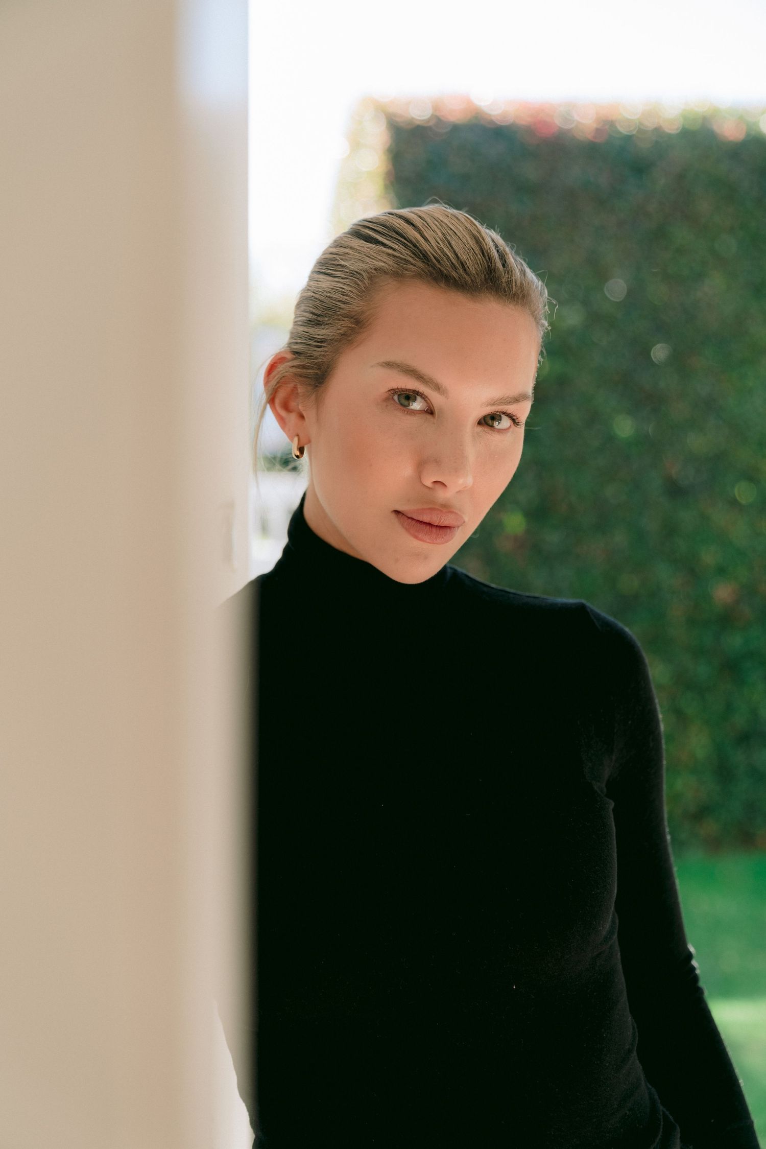 Portrait of a woman in a black turtleneck sweater against a blurred green garden backdrop.