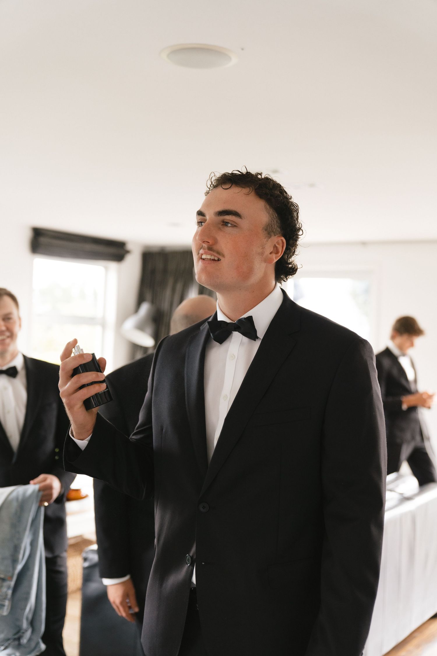 Men in formal black tuxedos and bow ties gather during wedding preparations.