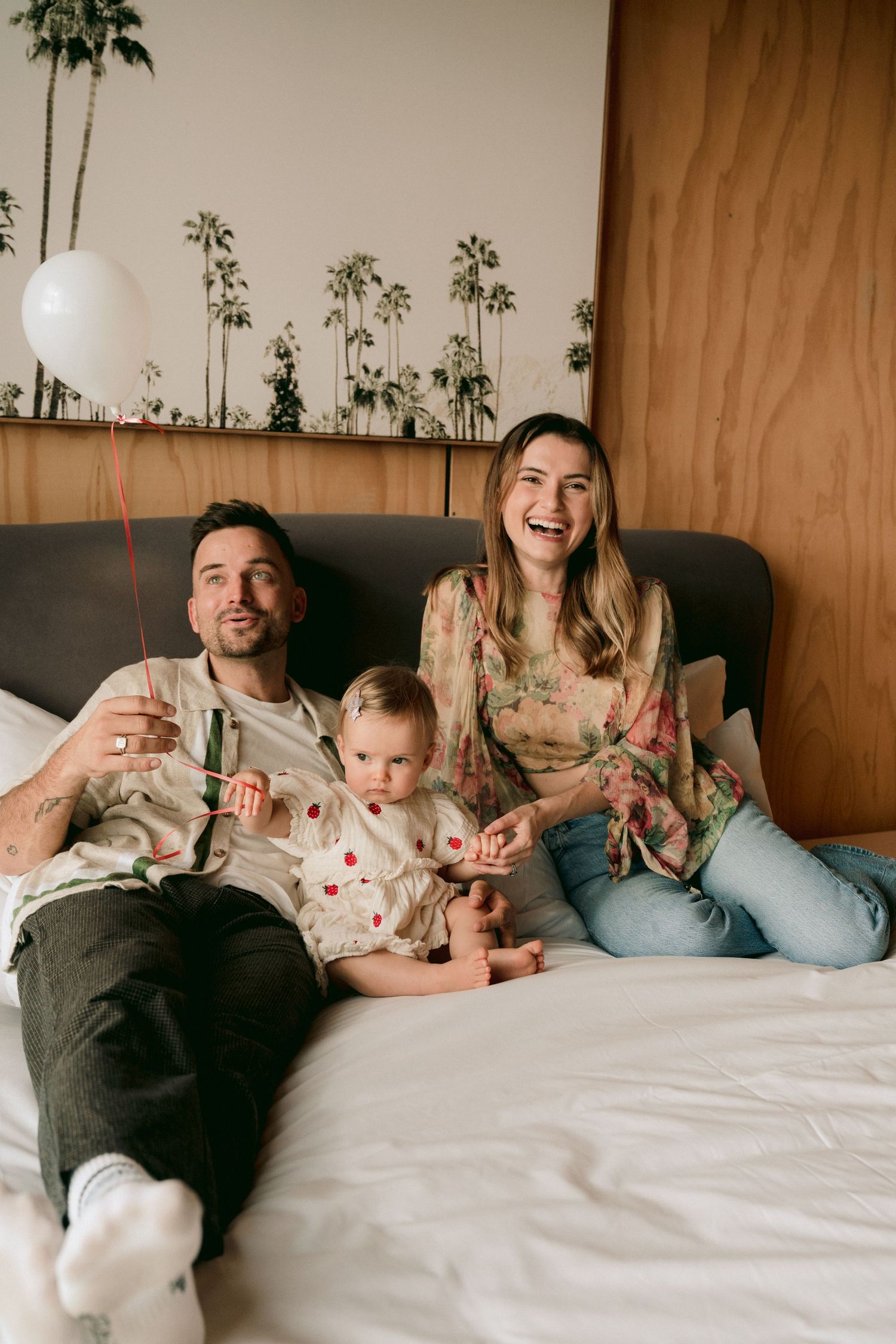 A family relaxes together on a couch, sharing joyful moments in a cozy room with decorative plants in the background.
